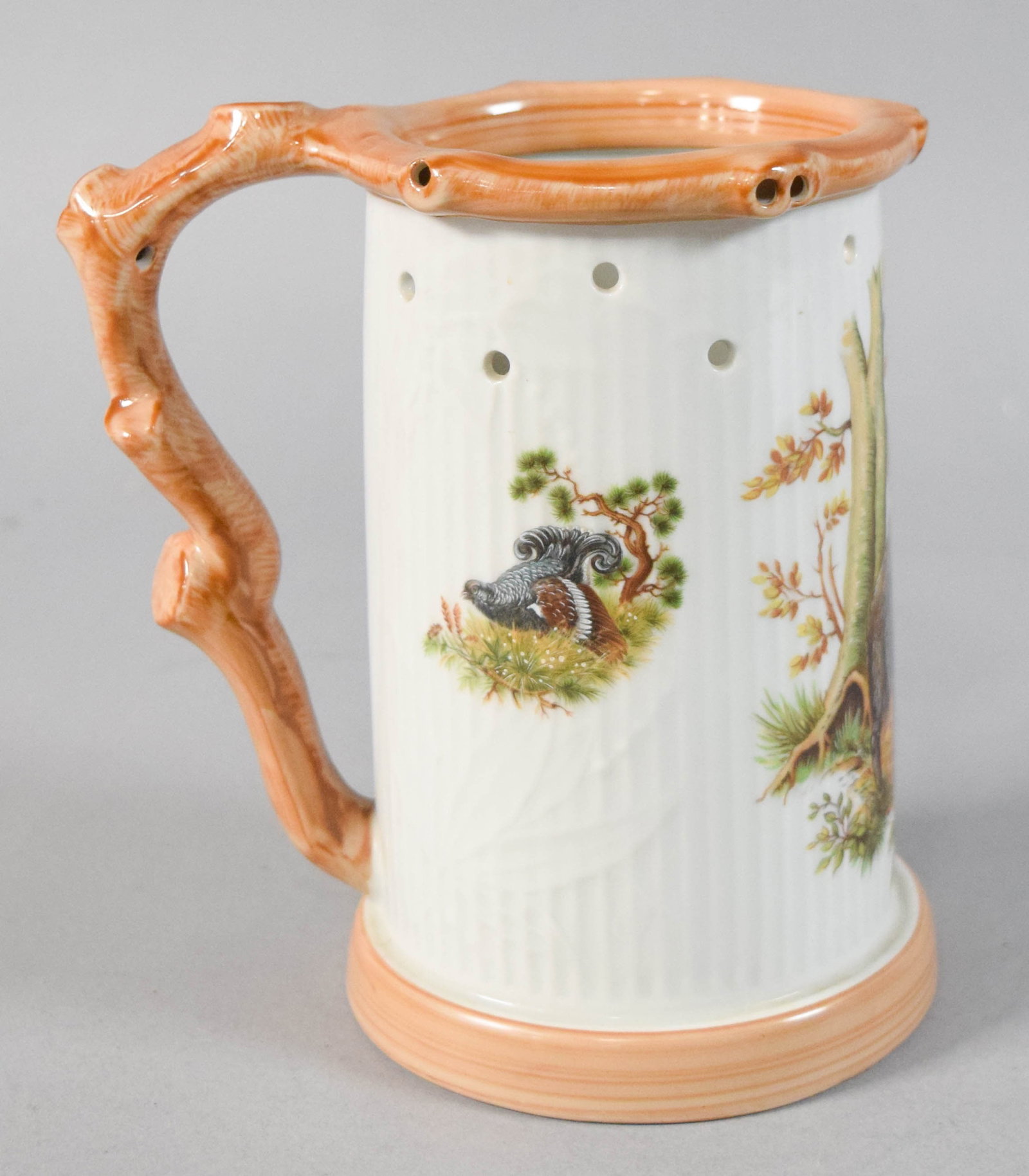 Glazed Ceramic Puzzle Mug With Wildlife Scenes: Glazed ceramic puzzle mug decorated with wildlife scenes and a sculpted branch handle. Underside is smooth and glazed, bearing no maker's marks or stamps. 7" H x 6 1/2" W x 4 3/4" D.