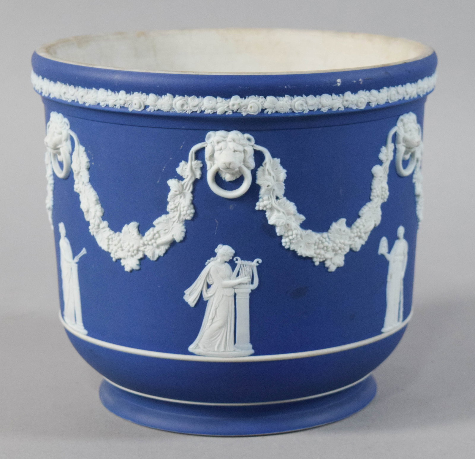 Wedgwood Cobalt Blue Jasperware Lion Head Jardiniere: Wedgwood cobalt blue jasperware jardiniere with lion head masks and swags of grape leaves and garlands. Underside marked Wedgwood and England. 7" H x 8 1/4" diameter.