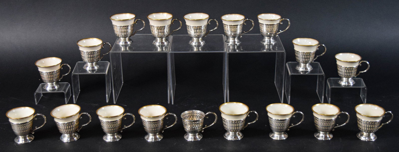 18 Sterling Demitasse Cup Holders with 17 Lenox Porcelain Liners: Set of 18 sterling silver demitasse cup holders with 17 porcelain liners. Silver holders with pierced openwork, and porcelain liners with gilt rims. Each porcelain liner marked Lenox on the base. Tota
