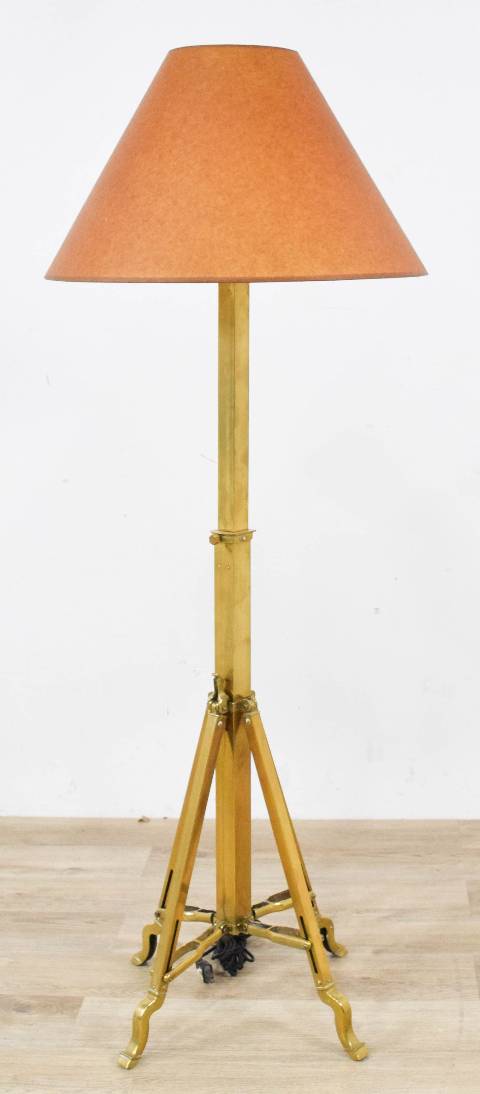 Adjustable Brass Tripod Floor Lamp: Adjustable brass tripod floor lamp with a sliding height-adjustment mechanism and large conical parchment-like shade. 56 1/2" H x 21" shade diameter.