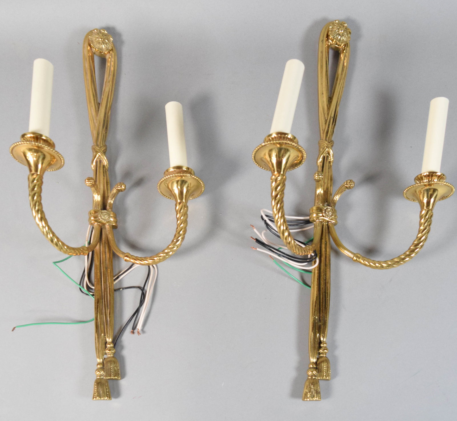 Pair of Neoclassical Style Brass Two-Light Wall Sconces: Pair of Neoclassical style brass two-light electric wall sconces. Two scrolled arms with a rope-twist motif extend from the center to support bobeches with beaded rims and plastic candle sleeves. The 