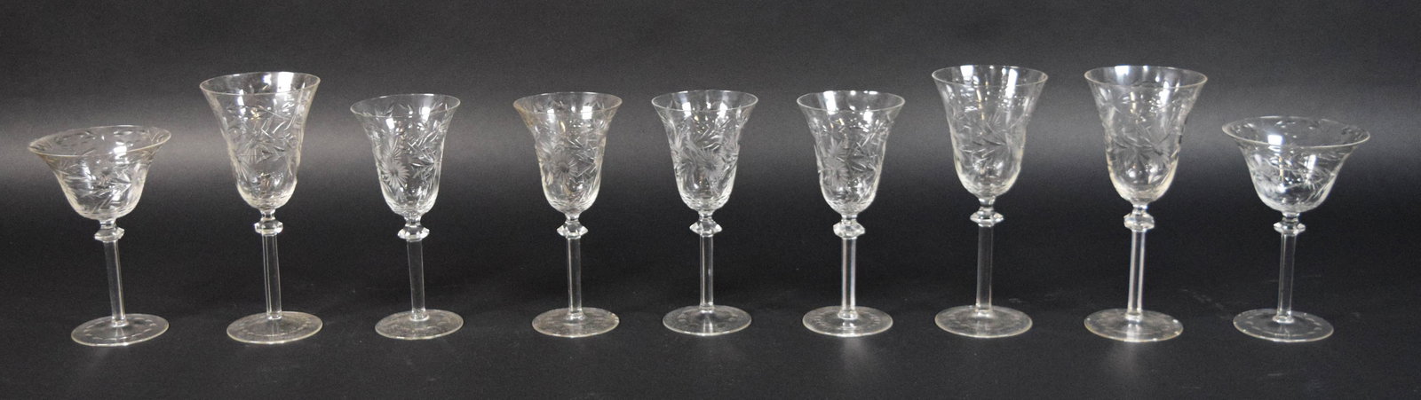 Collection of 9 Floral Cut Glass Stemware Pieces: Collection of nine clear cut glass stemware pieces featuring wheel-cut floral and foliate motifs. The group includes various sizes and forms, including flared goblets and wider coupe-style glasses. Al