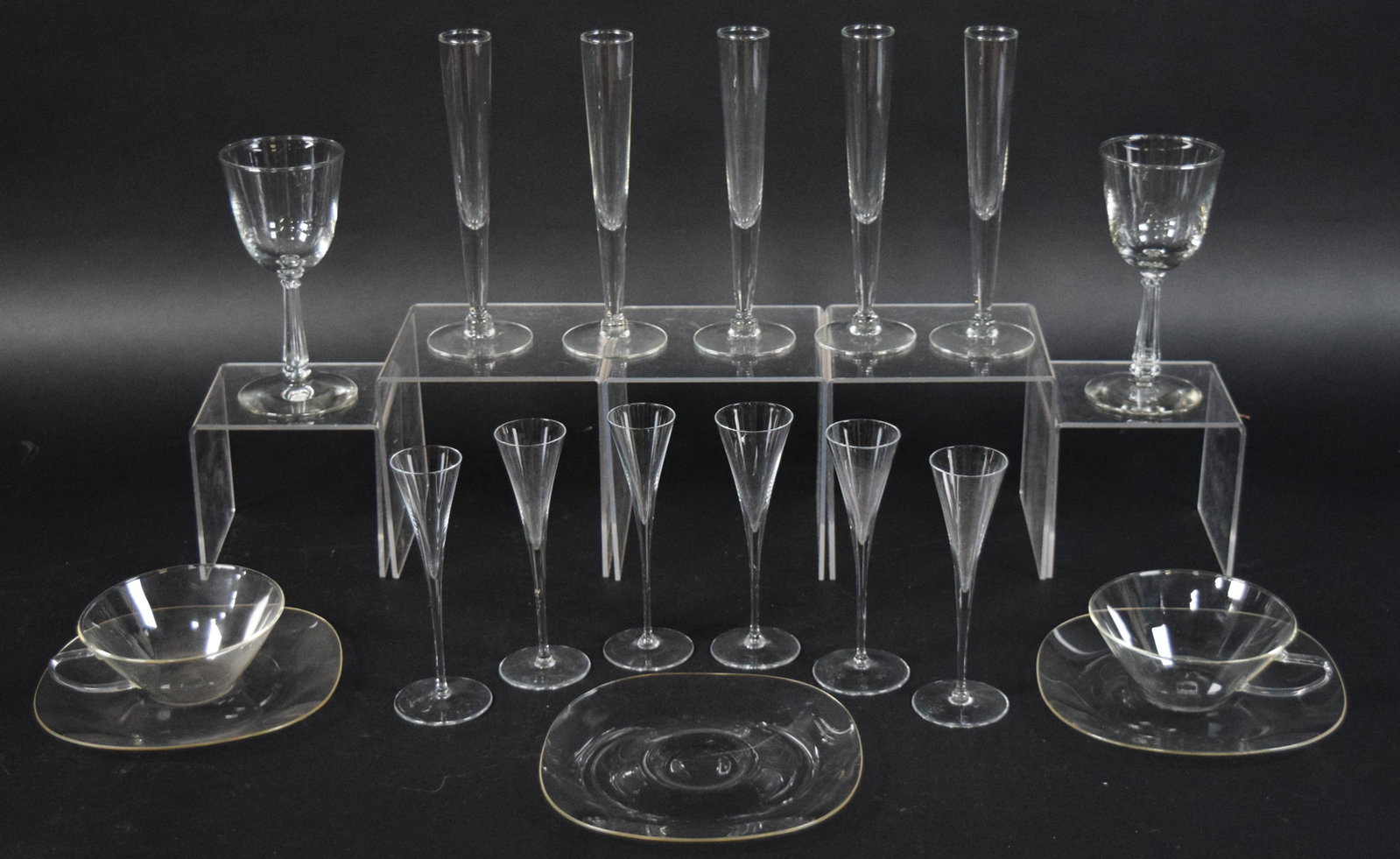 Collection of Schott Mainz Jenaer MCM Glassware: 18 pieces of Mid-Century Modern glassware by Schott Mainz Jenaer. Includes two wine goblets, five flutes, six bowl flutes, two teacups, and three saucers. Largest piece (flute) 7" H x 3 1/4" diameter.