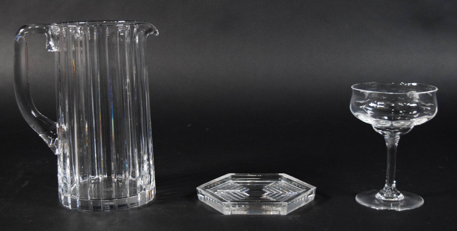 Group of 3 Baccarat Crystal Tableware Incl Harmonie Pitcher: Group of three pieces of Baccarat clear lead crystal. One tall, cylindrical water pitcher in the Harmonie pattern, signed on the underside of the base. One thick hexagonal coaster or small dish with a