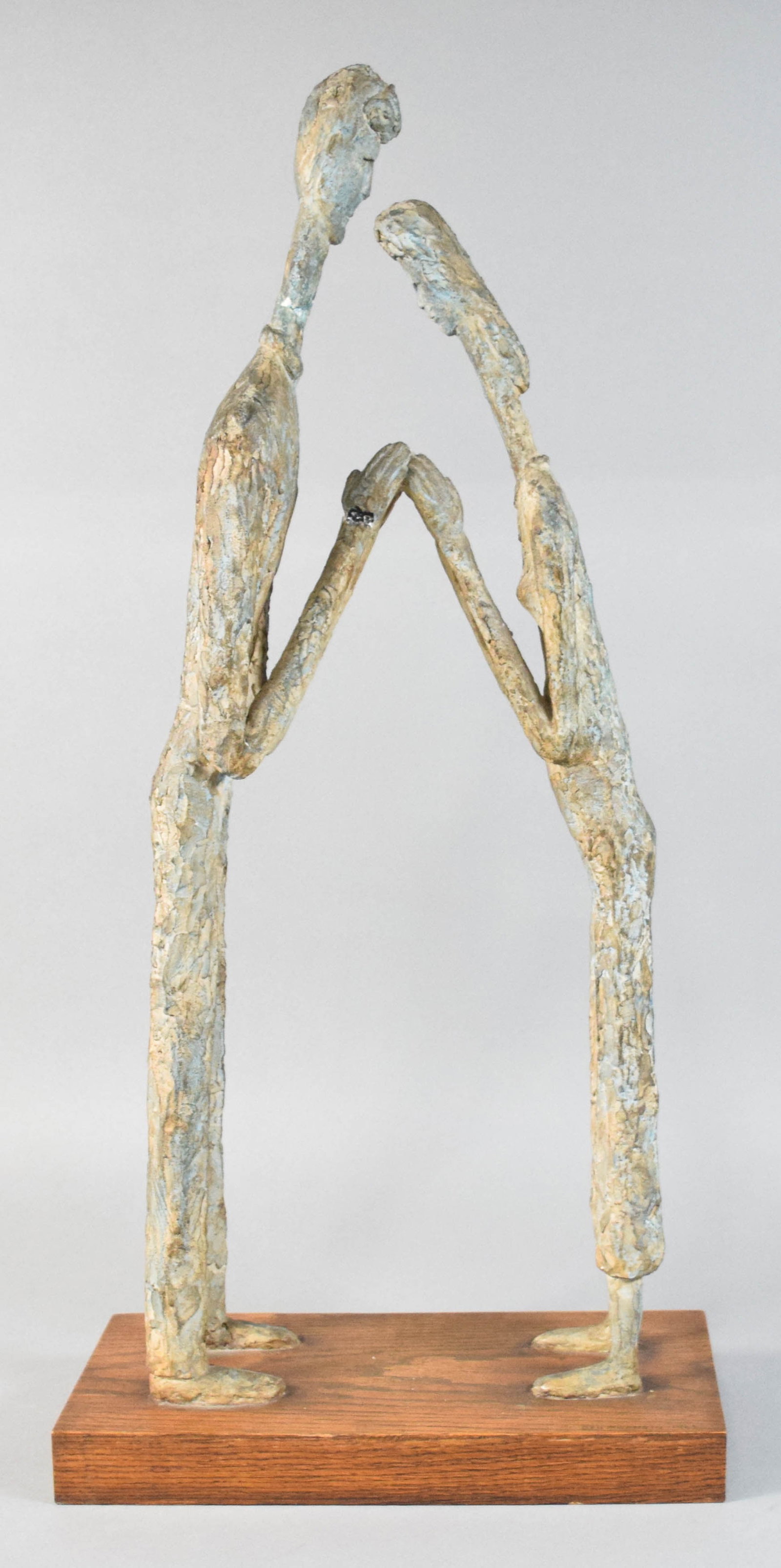 Ben Goodkin MCM Stylized Figurative Sculpture, 1964: Ben Goodkin (American, 20th Century). Mid-Century Modern stylized figurative sculpture with two elongated figures joining hands. The figures are rendered in a textured composite material with a varieg