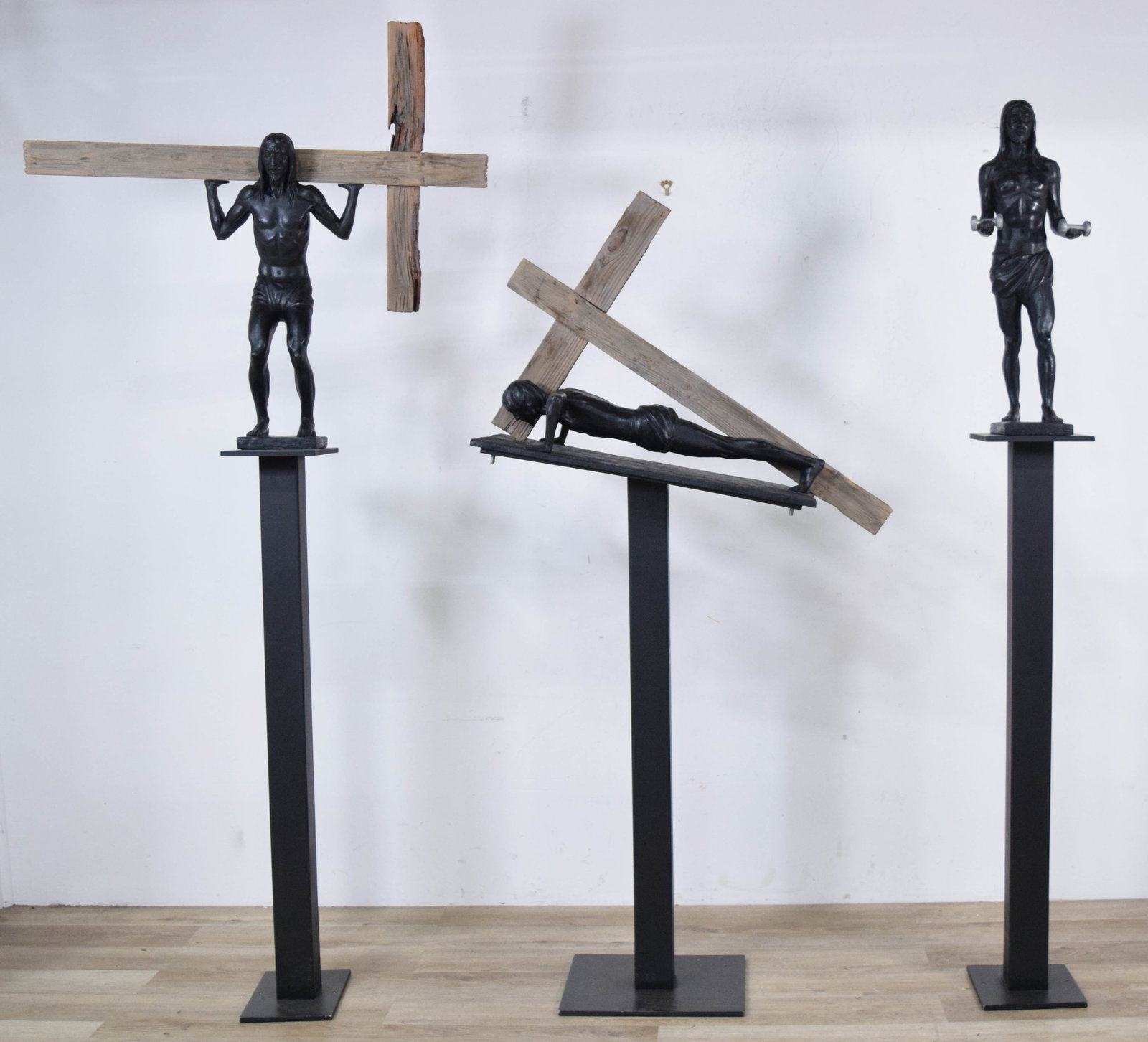 Trio of Contemporary Sculptures of Jesus Christ on Pedestal Stands: Trio of contemporary sculptures depicting Jesus Christ in various athletic and laborious poses, each mounted on a metal pedestal. Resin and terracotta. Two with weathered wooden crosses. Largest sculp