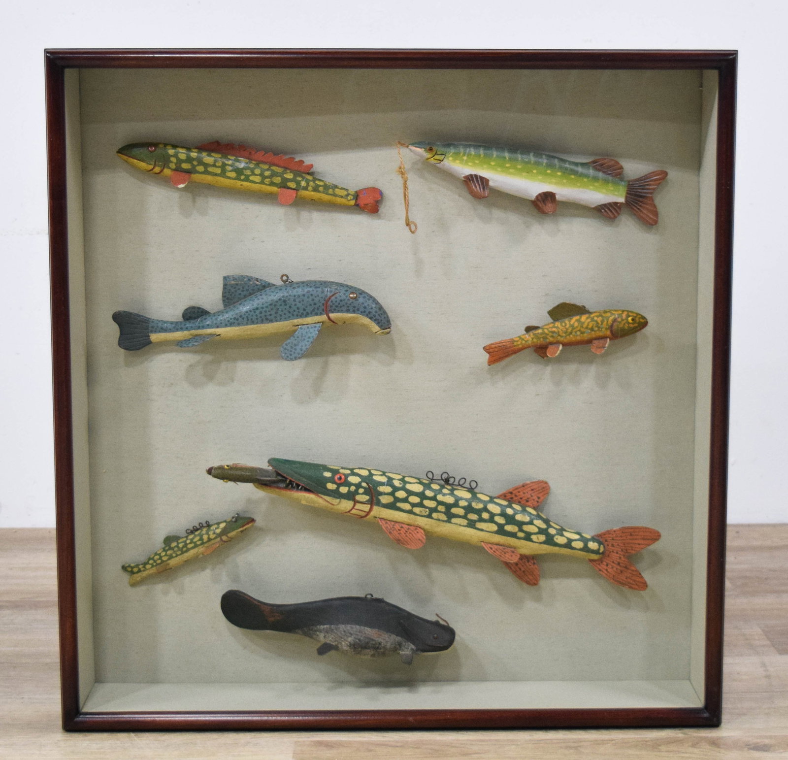 Collection of 7 Folk Art Fish Decoys by Swenarton: Collection of seven hand-carved and painted wooden fish decoys in a shadowbox. Wooden bodies, metal fins, and wire loops for suspension. Several signed Gordon Swenarton 1992. 30" H x 30 1/2" W x 5" D.