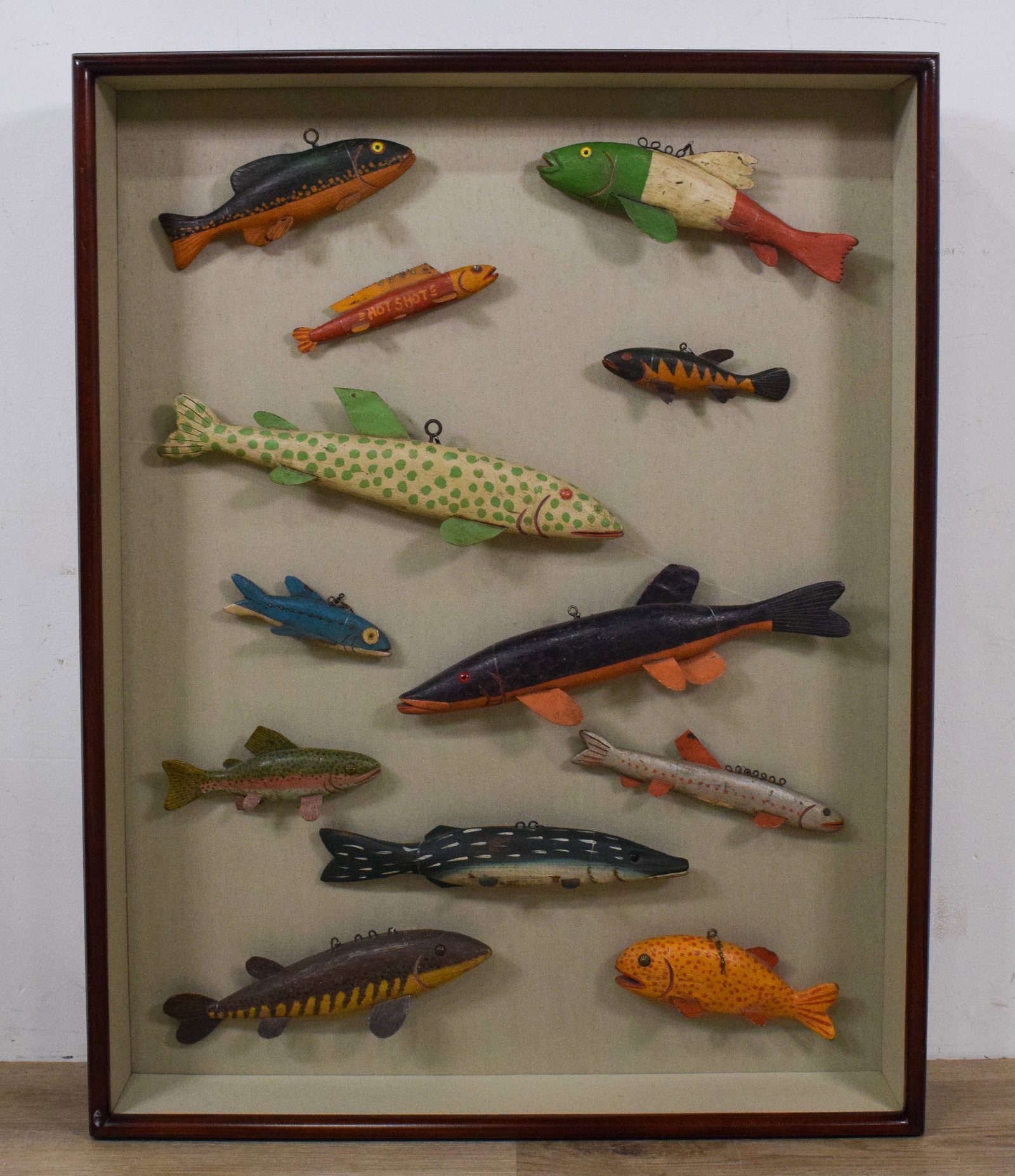 Collection of 12 Folk Art Fish Decoys by Swenarton: Collection of 12 hand-carved and painted wooden fish decoys in a shadowbox. Wooden bodies, metal fins, and wire loops for suspension. Several signed Gordon Swenarton 1992. One incised SRW - White. 39"