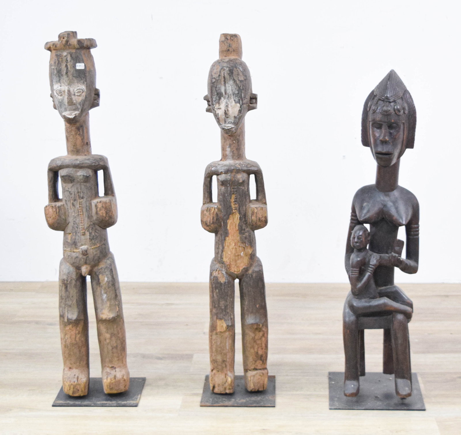 3 West African Style Carved Wood Figures: Group of three West African style carved wood figures including two standing figures and one seated maternity figure. All mounted on metal bases. Largest figure 35 1/2" H x 8 1/4" W x 8 1/4" D.