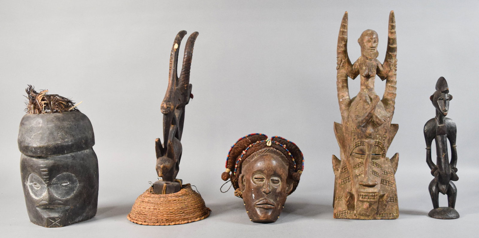 5 West African Ethnographic Masks and Figures: Group of five West African ethnographic objects including four masks or headdresses and one standing figure. Attributed to Mali, Cameroon, and Cote d'Ivoire. Several decorated with natural fibers, gla