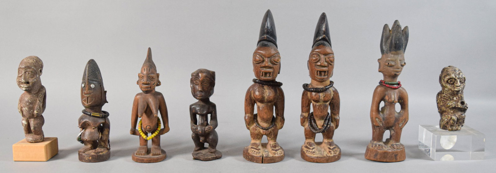 8 African Tribal Style Carved Figures: Group of eight figurative sculptures in various African tribal styles, including wood carvings and two figures made of a stone or clay-based material. Materials used for embellishment include inset ey
