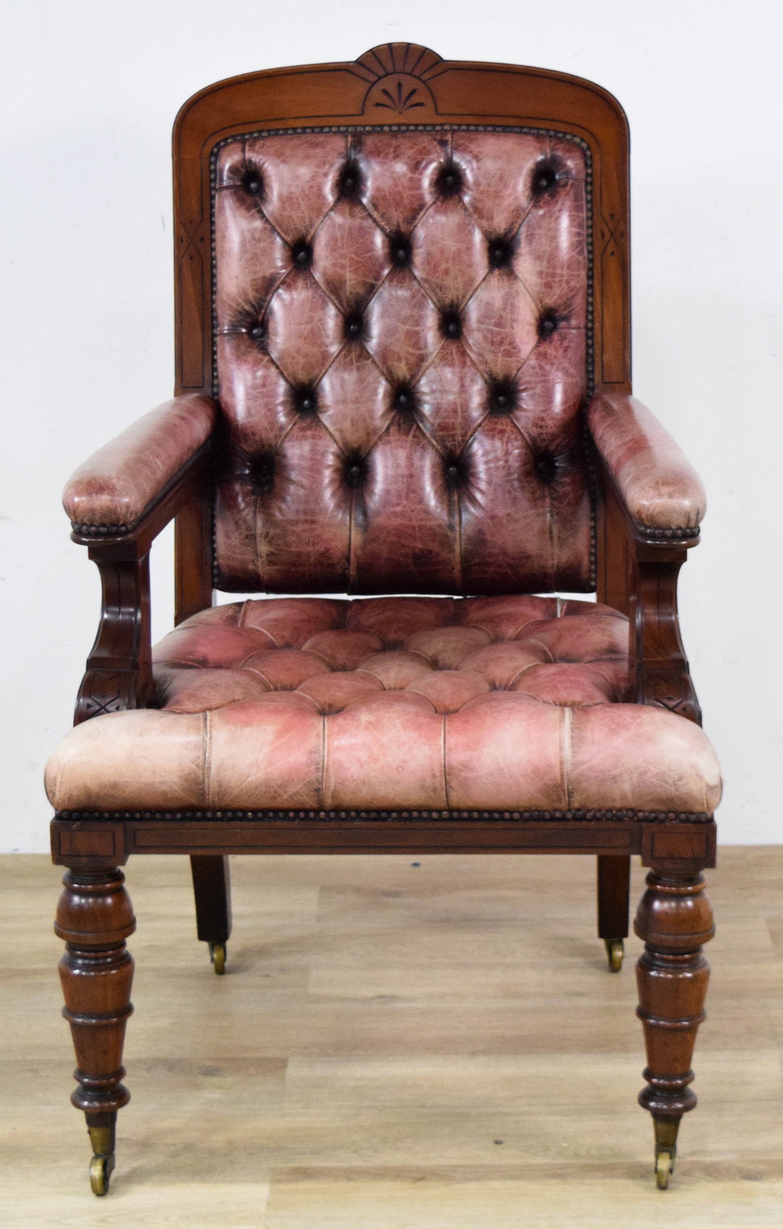 Victorian Aesthetic Movement Library Armchair: Victorian Aesthetic Movement carved hardwood and tufted leather library armchair. Tufted burgundy leather upholstery with brass nailhead trim. Two front turned legs and two splayed back legs, all on b