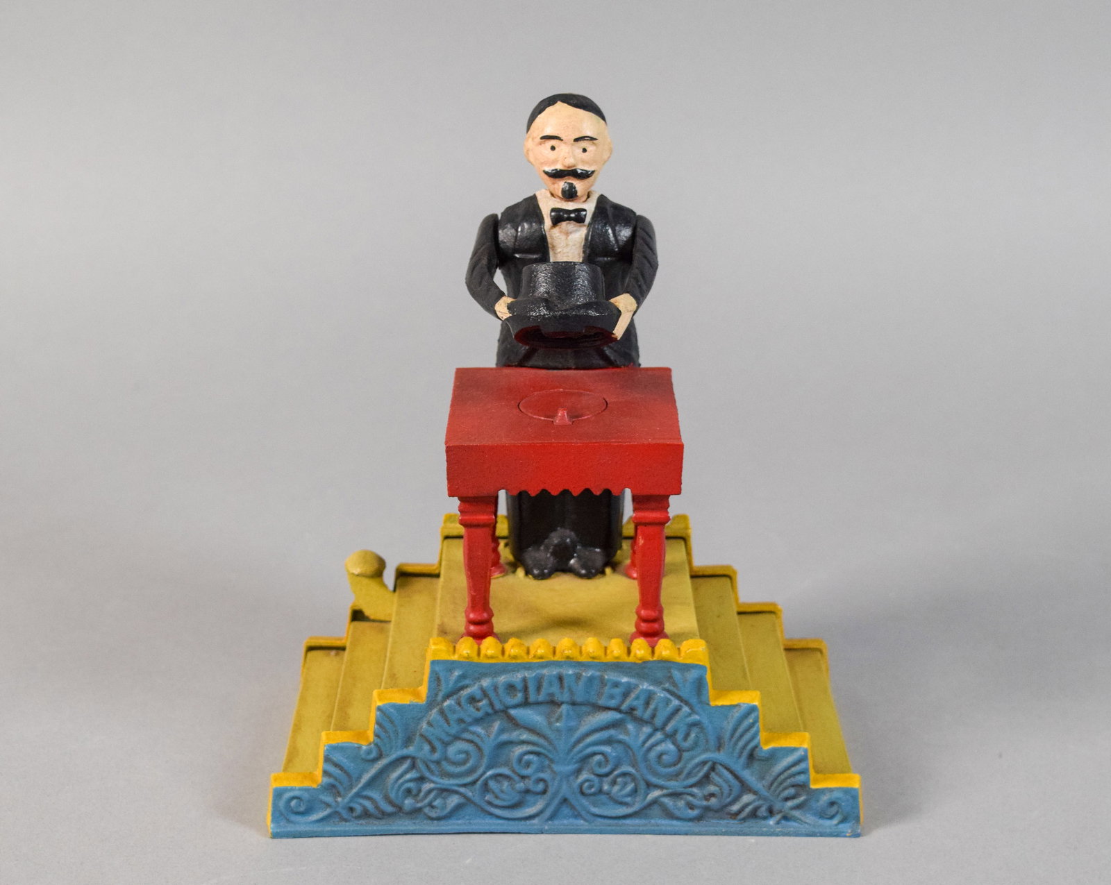 Cast Iron Repro Magician Mechanical Bank After J&E Stevens: Cast iron mechanical magician bank, reproduction of a late 19th-century design by J&E Stevens. Lever mechanism tested and working. Coin trap embossed Patd Feb 2 1882. 8" H x 7" W x 4" D.