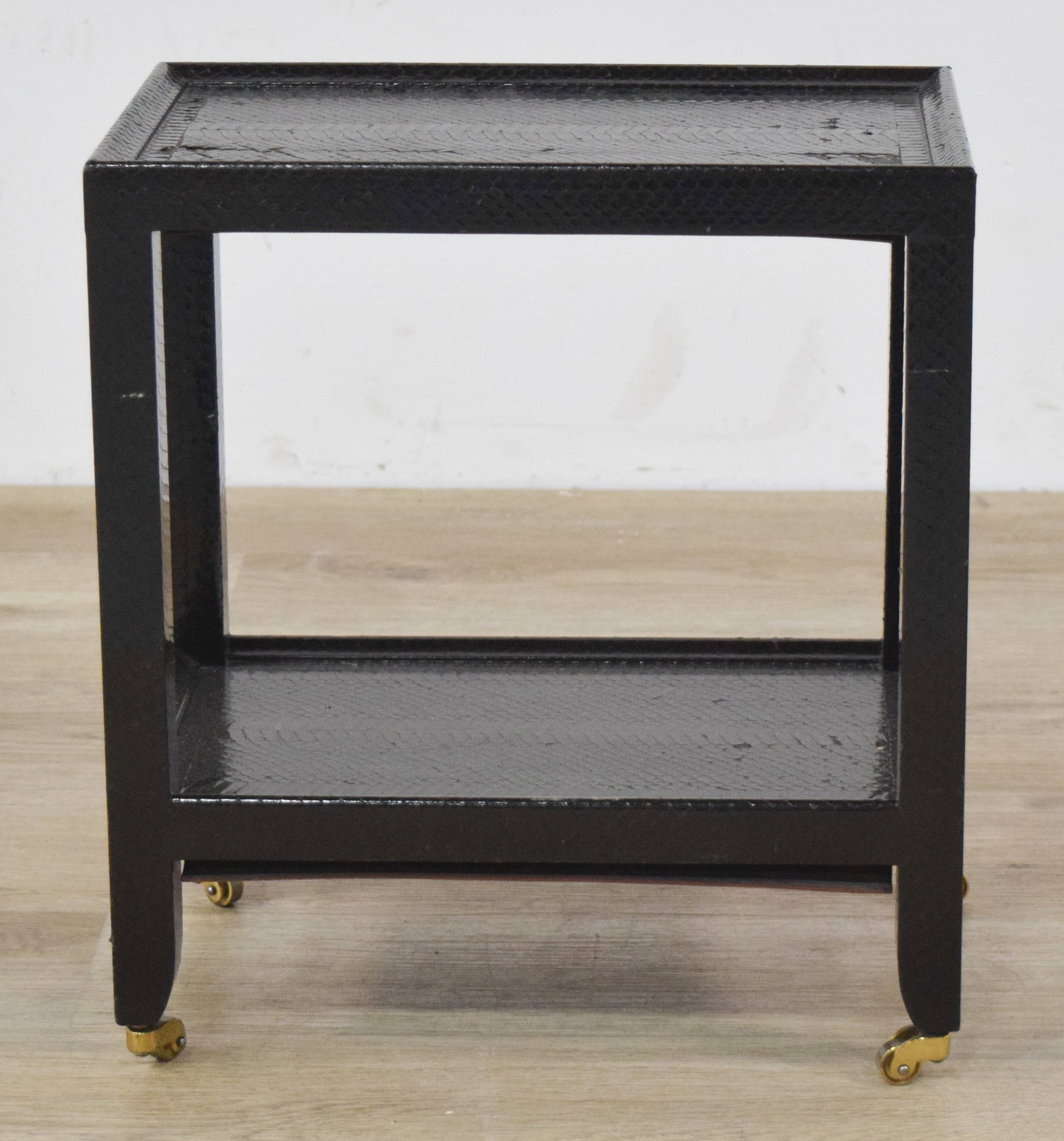 Signed Karl Springer Two-Tier Side Table: Small, embossed two-tier side table on brass casters. Underside marked with paper label signed Karl Springer 1989. 16" H x 9 1/2" W x 14 1/2" D.