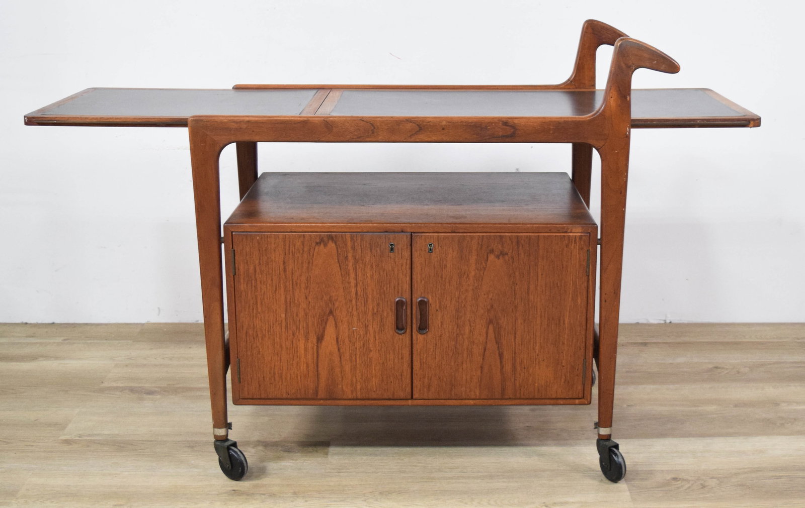 MCM Rolling Bar Cart with Drop-Leaf: Mid-century modern rolling bar cart with sculptural handles and a drop-leaf. Lower section with two-door cabinet mounted on casters. 36" H x 34 1/2" W x 19 1/2" D.