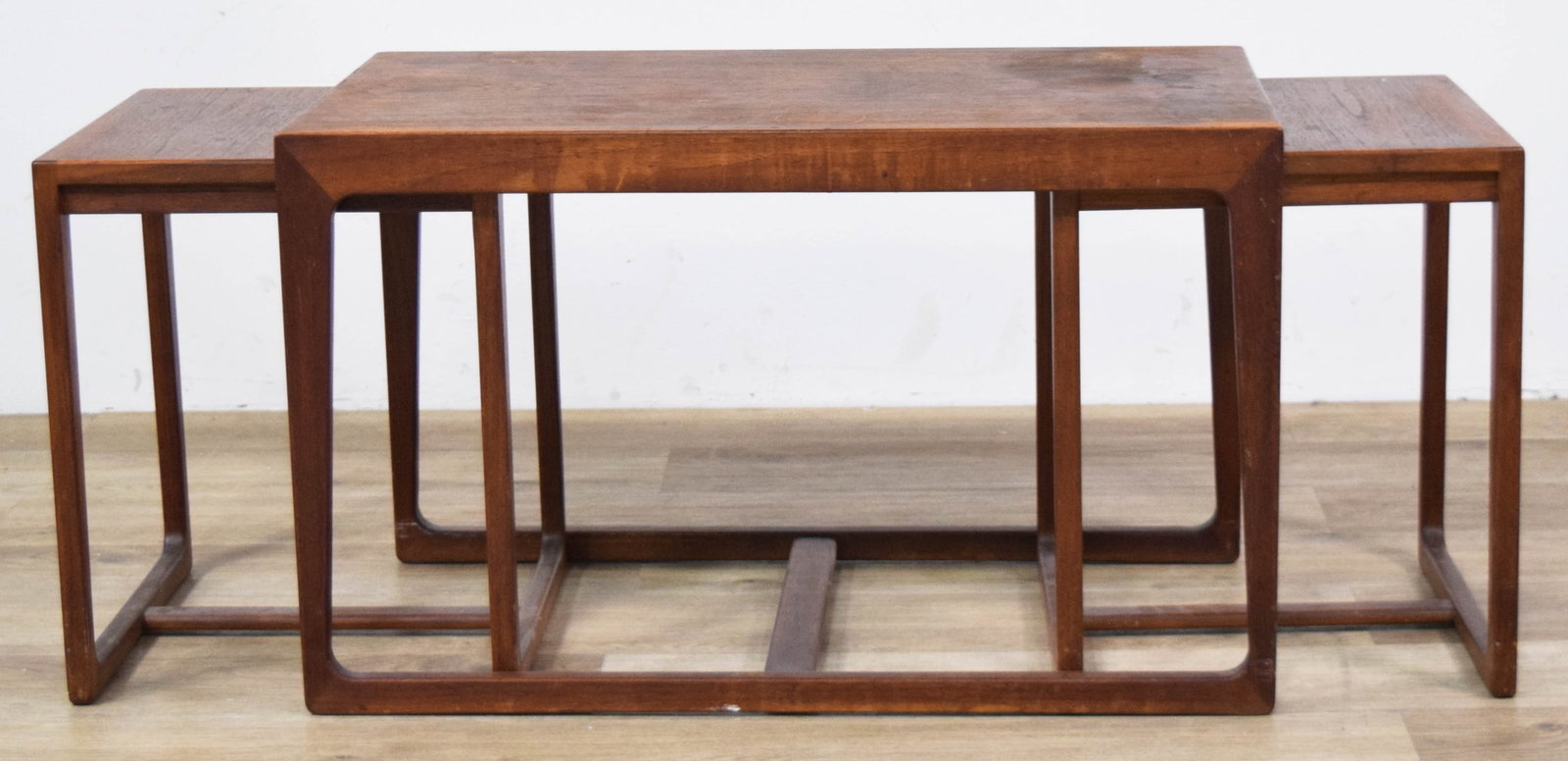 3 MCM Teak Nesting Tables: Three Mid-Century Modern teak nesting tables in the Danish modern style. Trio consists of one primary rectangular table and two smaller square tables nesting inside the larger frame. Largest table 17 