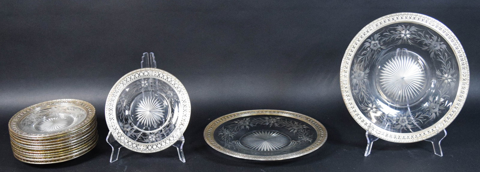 14-Piece Set of Cut and Etched Glass Tableware: Group of 14 cut and etched glass tableware items including one large platter, one medium plate, and 12 small plates with sunburst designs and silver-plated rims. Largest piece (platter) 14" diameter.