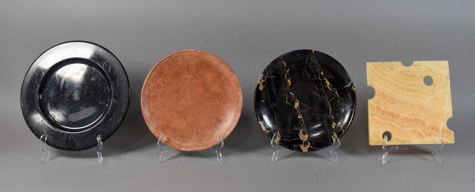 Group of 4 Stone and Marble Serving Platters: Group of four carved and polished stone and marble plates and platters. Includes a large round black stone charger; a shallow reddish-brown stone charger with a porous, travertine-like texture; a poli