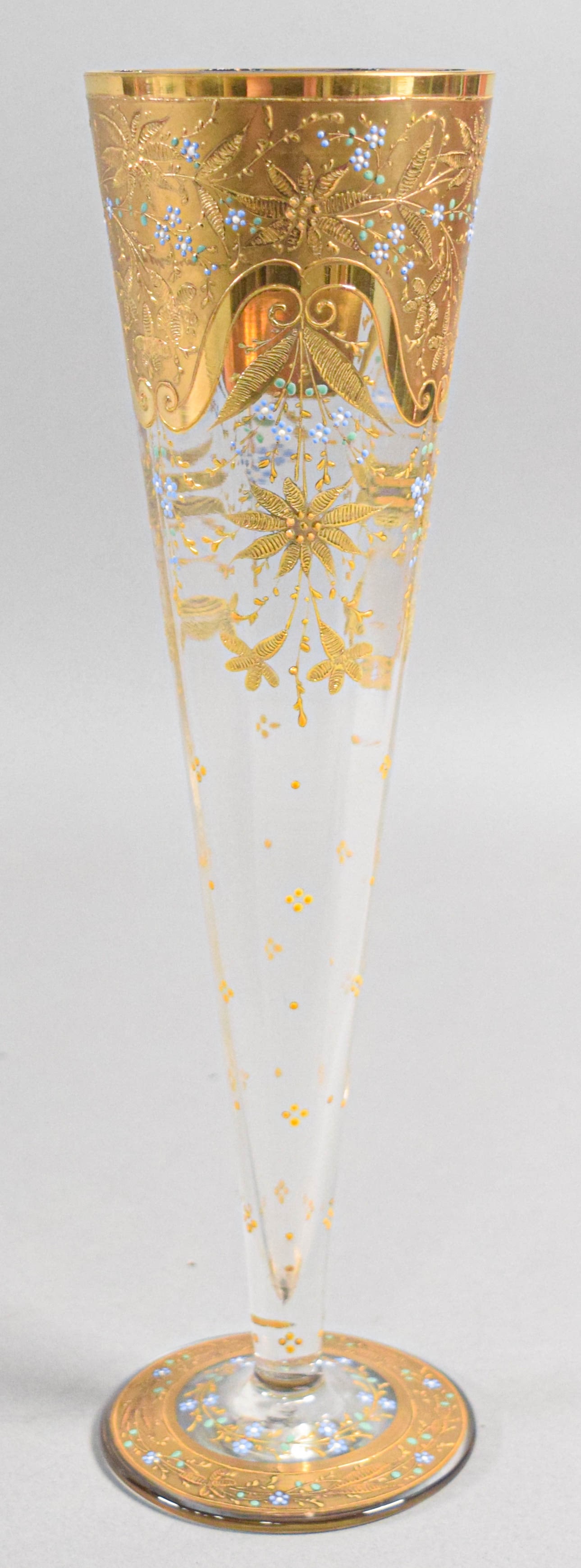 Bohemian Gilded and Enameled Faceted Glass Trumpet Vase: This trumpet-form vase is composed of clear faceted glass with an eight-paneled body tapering to a narrow stem on a circular spreading foot. The upper portion features a wide band of raised gold relie