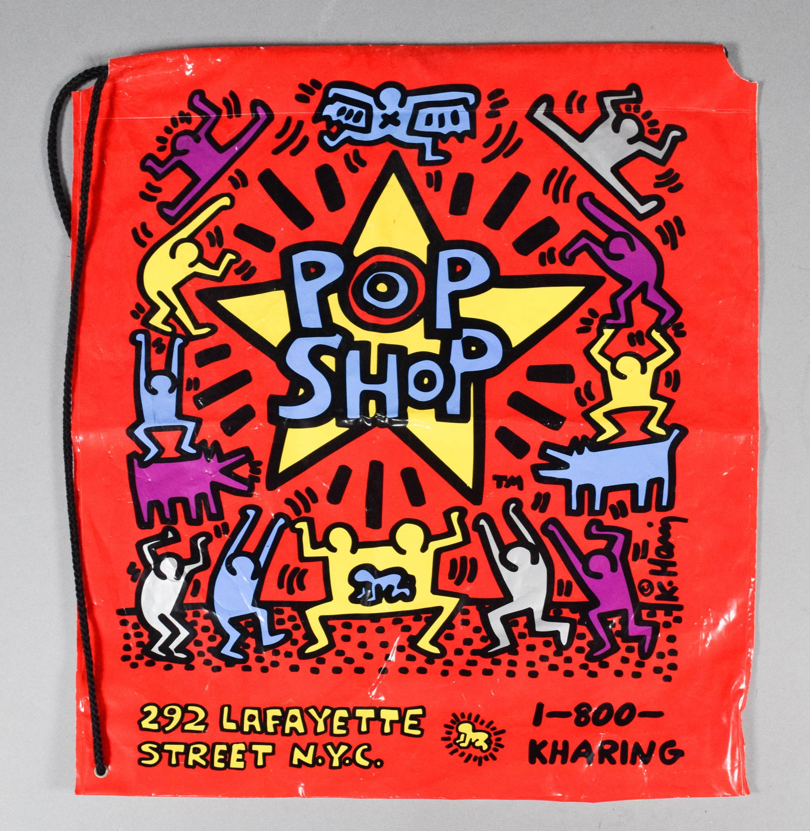 Keith Haring Pop Shop Screenprinted Plastic Drawstring Bag: A double-sided screenprinted plastic drawstring bag from Keith Haring's Pop Shop. Text printed on the red side includes the artist's name, the shop address 292 LAFAYETTE STREET N.Y.C., 1-800-KHARING, 