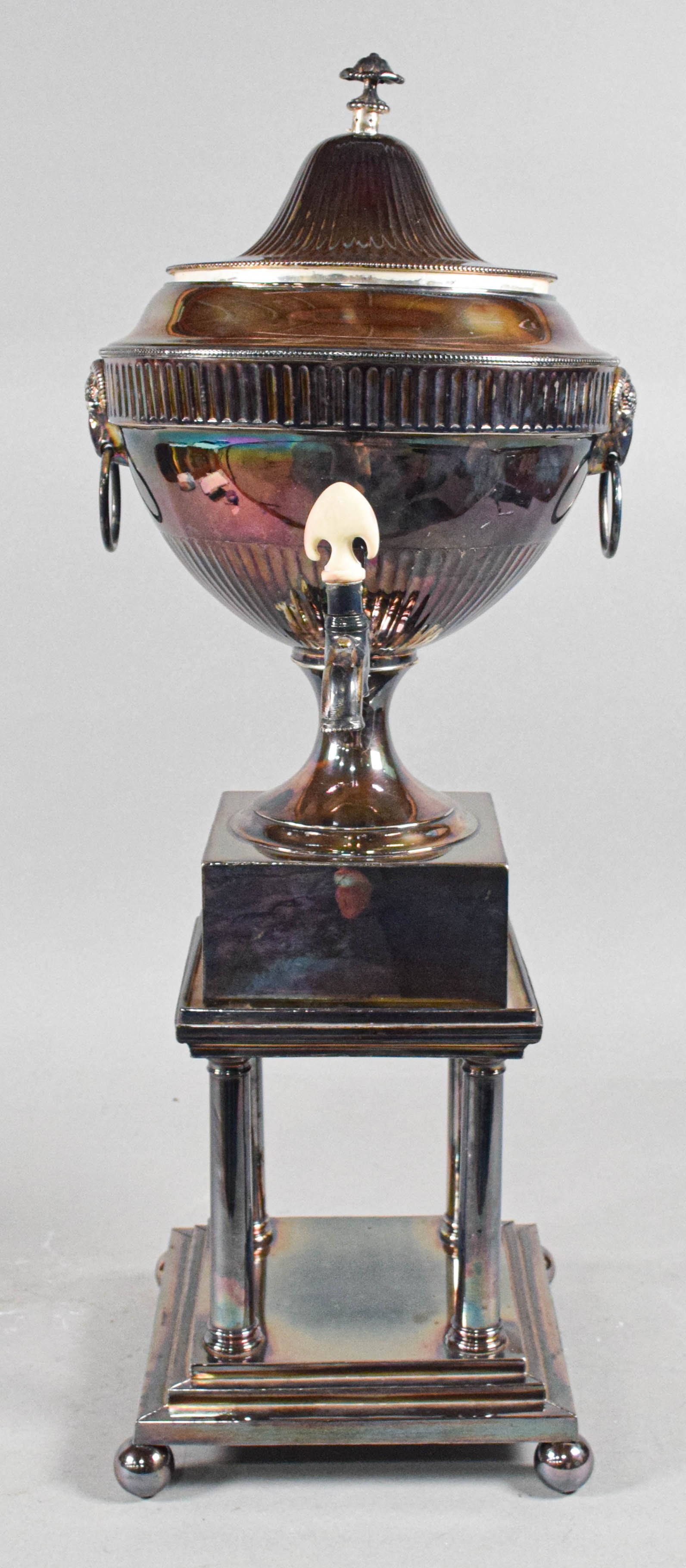 Neoclassical Style Silver Plated Samovar on Pedestal Stand: A Neoclassical style silver-plated hot water urn or samovar on a separate matching pedestal stand. The fluted urn body features ram's head handles with drop rings, a domed lid with a foliate finial, a