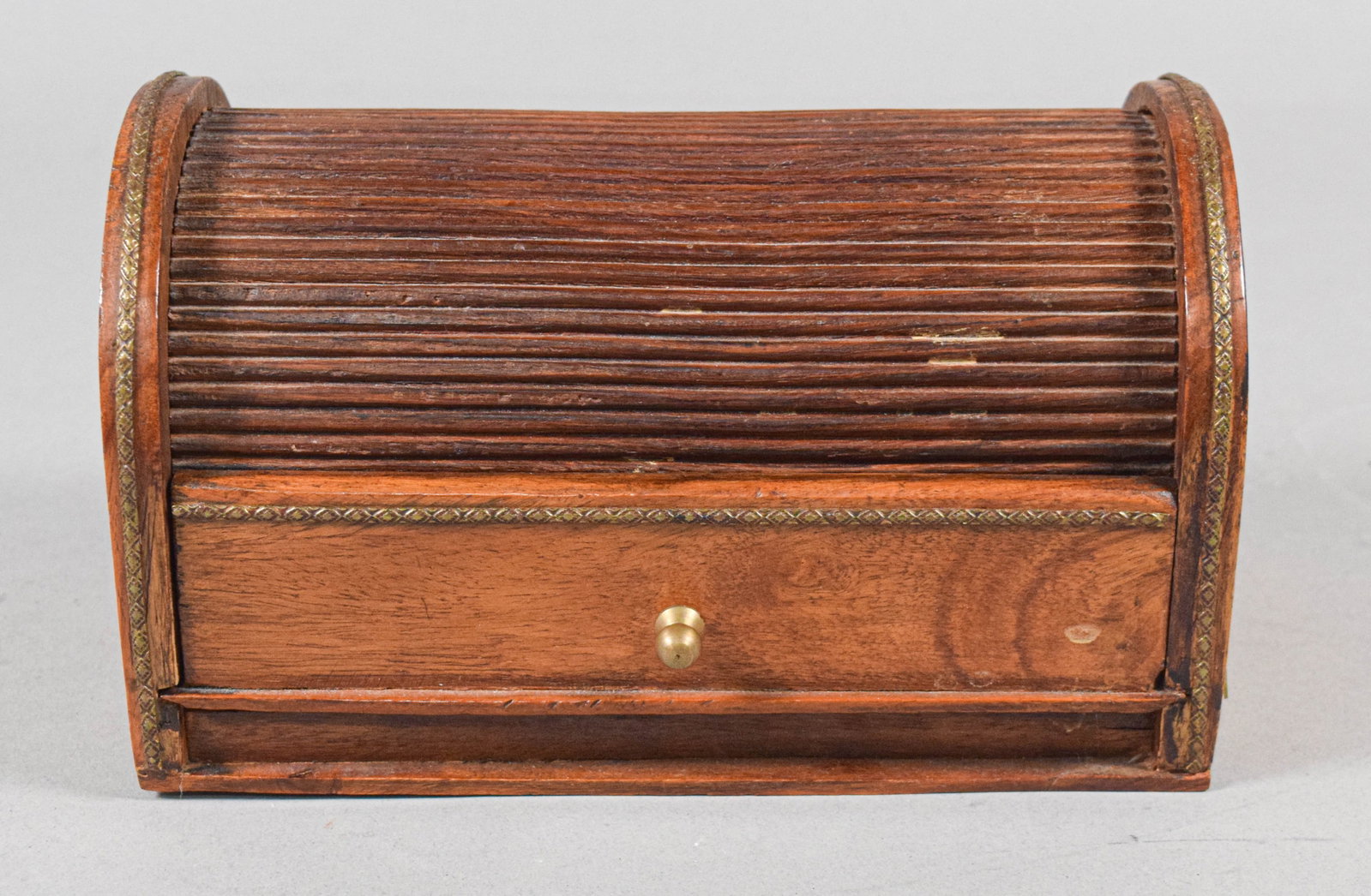 English Walnut Tambour Desk Box with Brass Inlay: This walnut desk box, circa 1900, features an arched silhouette with a retractable tambour slatted lid and a single lower drawer. The side panels are decorated with inlaid brass wire and sheet metal i