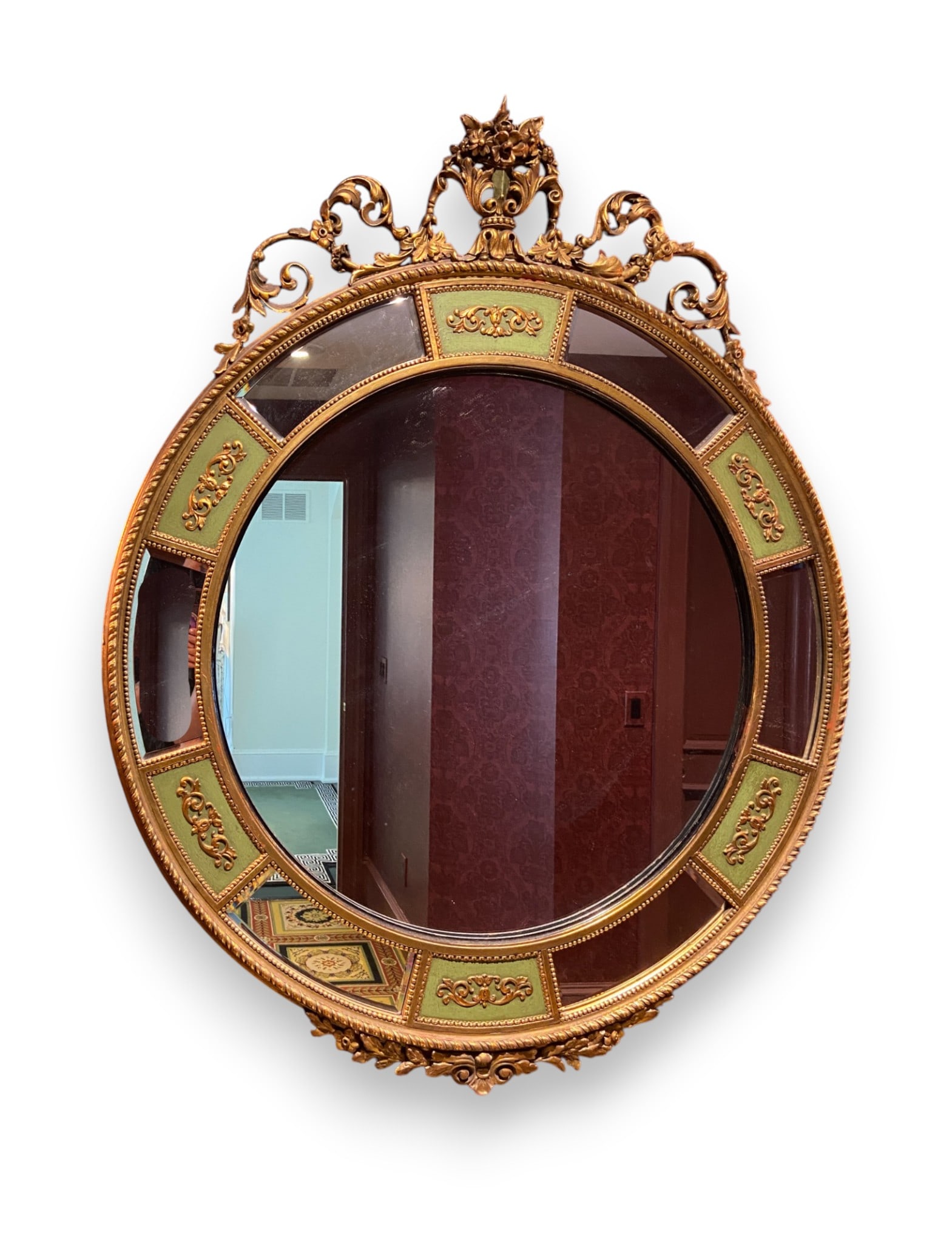 Large Neoclassical Style Gilded Oval Wall Mirror with Segmented Border: This is a large Neoclassical revival style wall mirror of oval form. The frame is constructed of wood and composition with a gilded finish over a red bole base. The design features an elaborate crest 