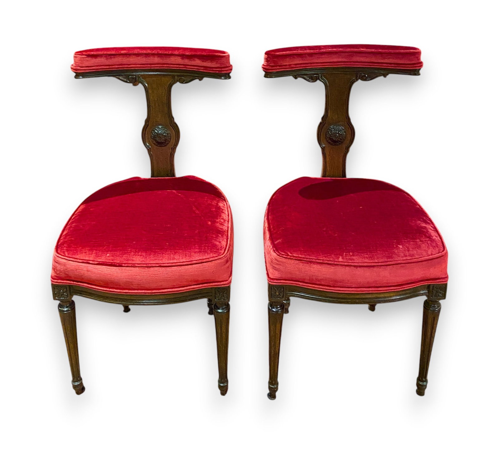 A Pair of Louis XVI Style Mahogany and Red Velvet Cockfighting Chairs: This pair of chairs is designed in the Louis XVI Neoclassical style. Each chair features a T-shaped backrest with a curved, padded top rail supported by a shaped splat. The splat is decorated with a c