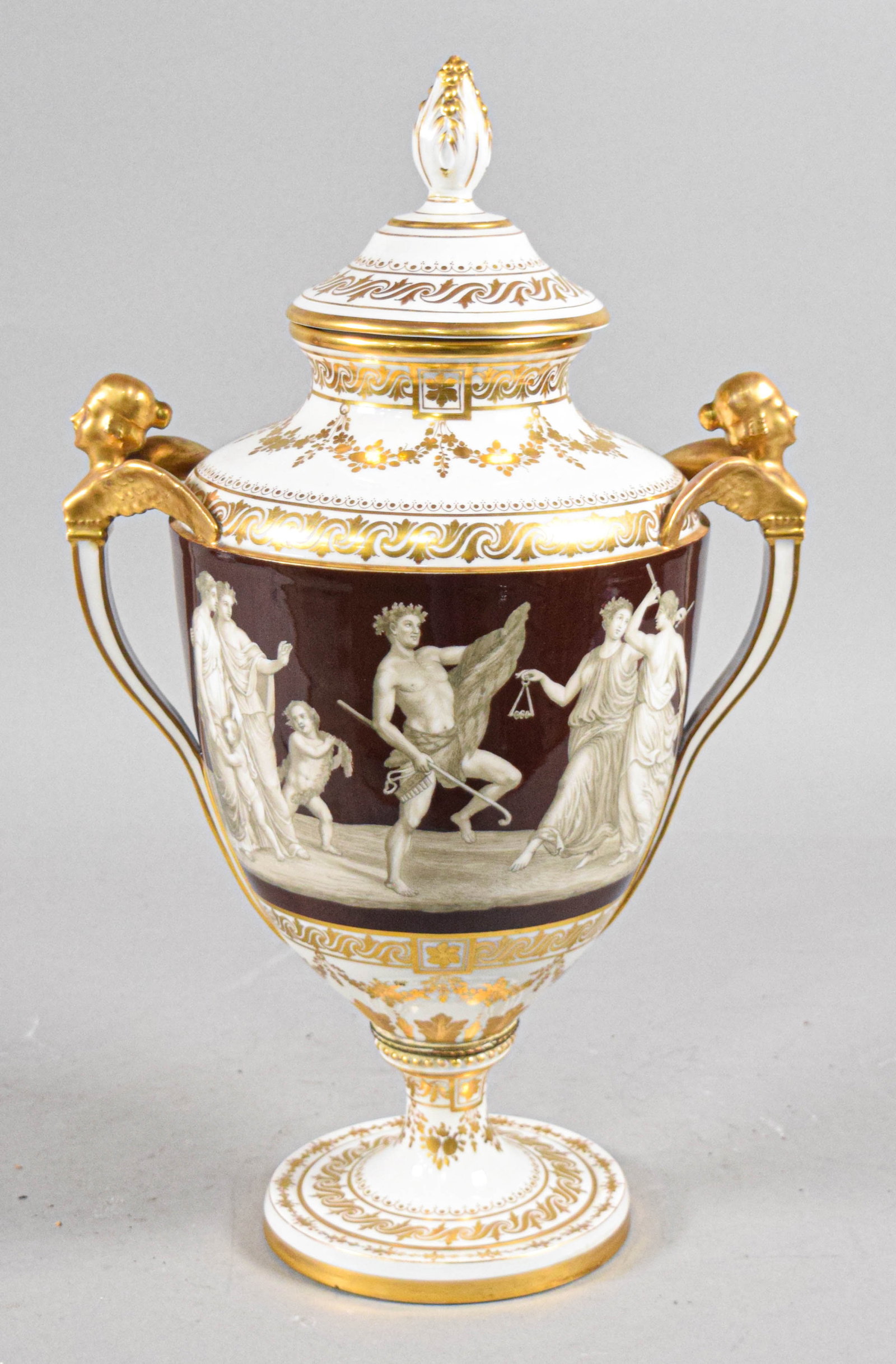 Imperial Vienna Style Porcelain Neoclassical Covered Urn: A large Imperial Vienna style porcelain covered urn of ovoid form, resting on a pedestal foot. The central body features a wide frieze in a deep maroon ground, decorated with a hand-painted classical 