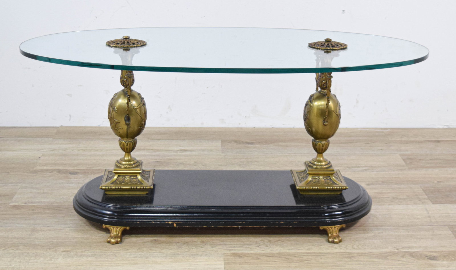 Large Classical Revival Style Bronze and Glass Oval Coffee Table: This large-scale coffee table is designed in the Classical Revival style. It features a thick, beveled oval glass top supported by two ornate cast bronze pedestals. The pedestals are fashioned as hand