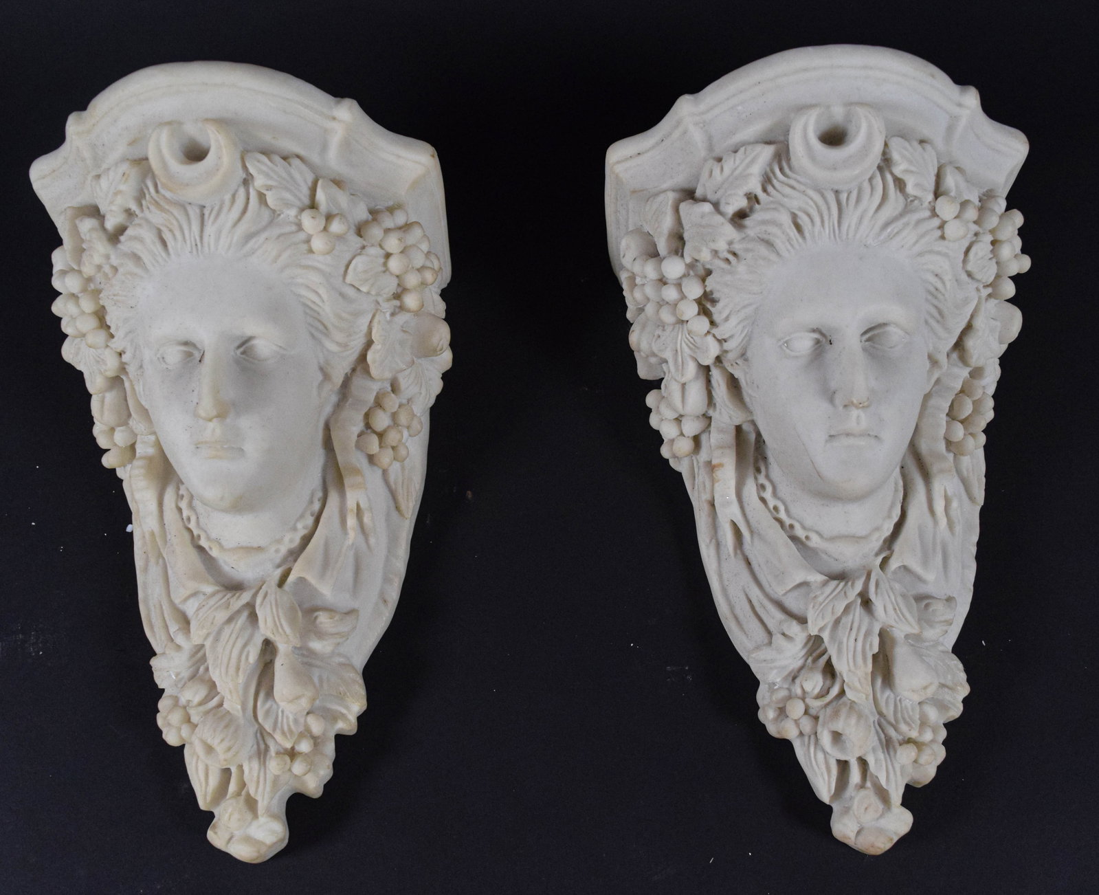 Pair of Neoclassical Style Female Mask Wall Corbels: A pair of molded plaster Neoclassical style wall corbels or brackets. Each corbel features a high-relief female mask positioned below a flat, molded top shelf. The figures are decorated with abundant 