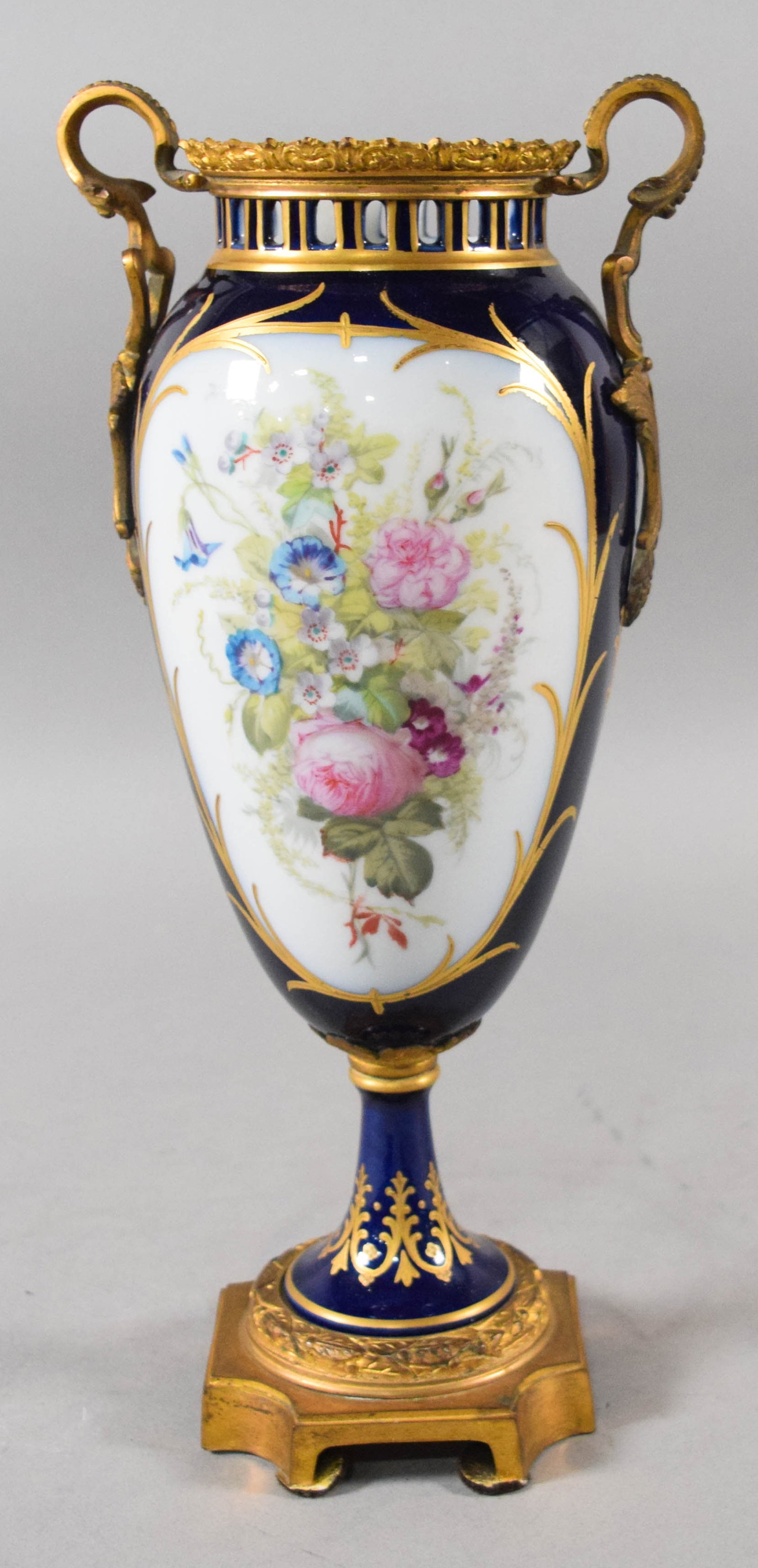 French Sevres Style Porcelain Amphora Vase with Ormolu Mounts: A late 19th-century French Sevres-style porcelain amphora-form vase featuring a rich cobalt blue ground and gilt-bronze ormolu mounts. The body is decorated with two large, hand-painted white reserves