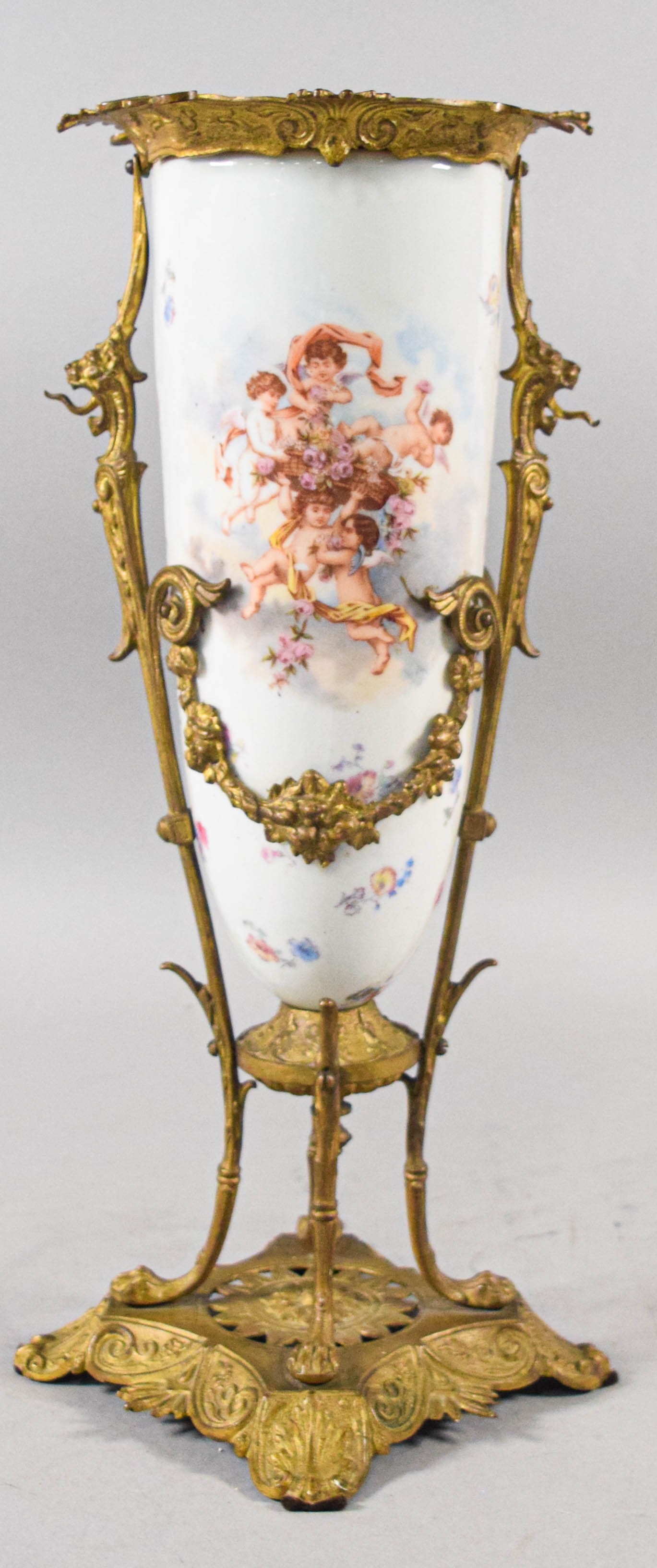 Sevres Style Porcelain and Gilt Bronze Vase with Cherub Scenes: This Sevres style porcelain vase is mounted in an elaborate gilt bronze or ormolu frame. The tall, ovoid porcelain body is finished in a white ground and decorated on both sides with hand-painted vign