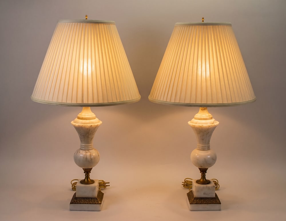 A Pair of Neoclassical Carved Alabaster Table Lamps: A matched pair of table lamps featuring carved white alabaster bodies with natural tan and grey veining. The lamps are designed in a neoclassical style, with a central urn-shaped stem set upon a squar