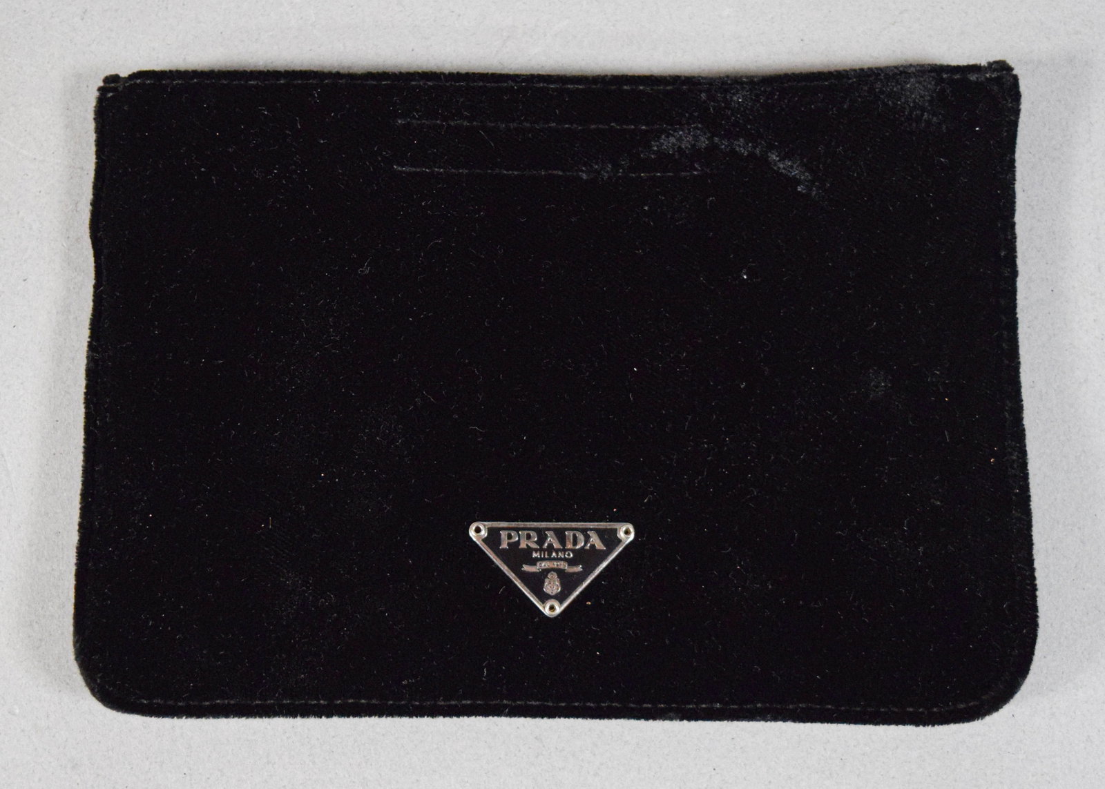 Prada Black Velvet Pouch with Authenticity Card: Prada black velvet pouch with velcro closure. Marked Prada Milano on the signature triangular front plaque. Interior lined with repeating logo pattern. Includes authenticity certificate card. 4 3/4" H