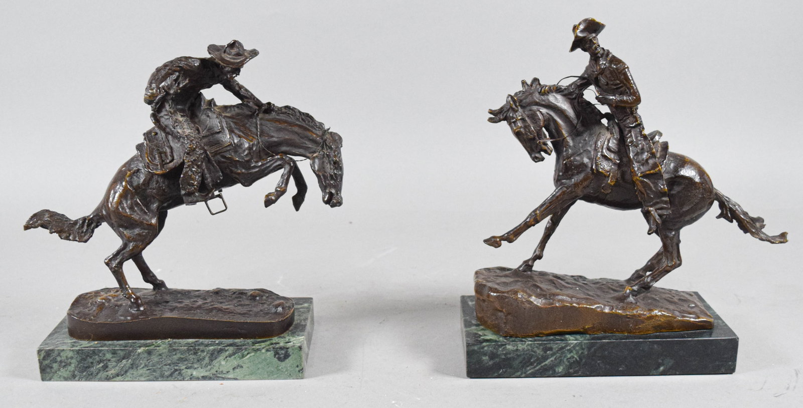 Pair of Frederic Remington Bronze Cowboy Sculptures: A pair of cast bronze sculptures after the Western works of Frederic Remington. One sculpture represents The Bronco Buster, depicting a cowboy in chaps clutching the mane of a bucking horse. The secon
