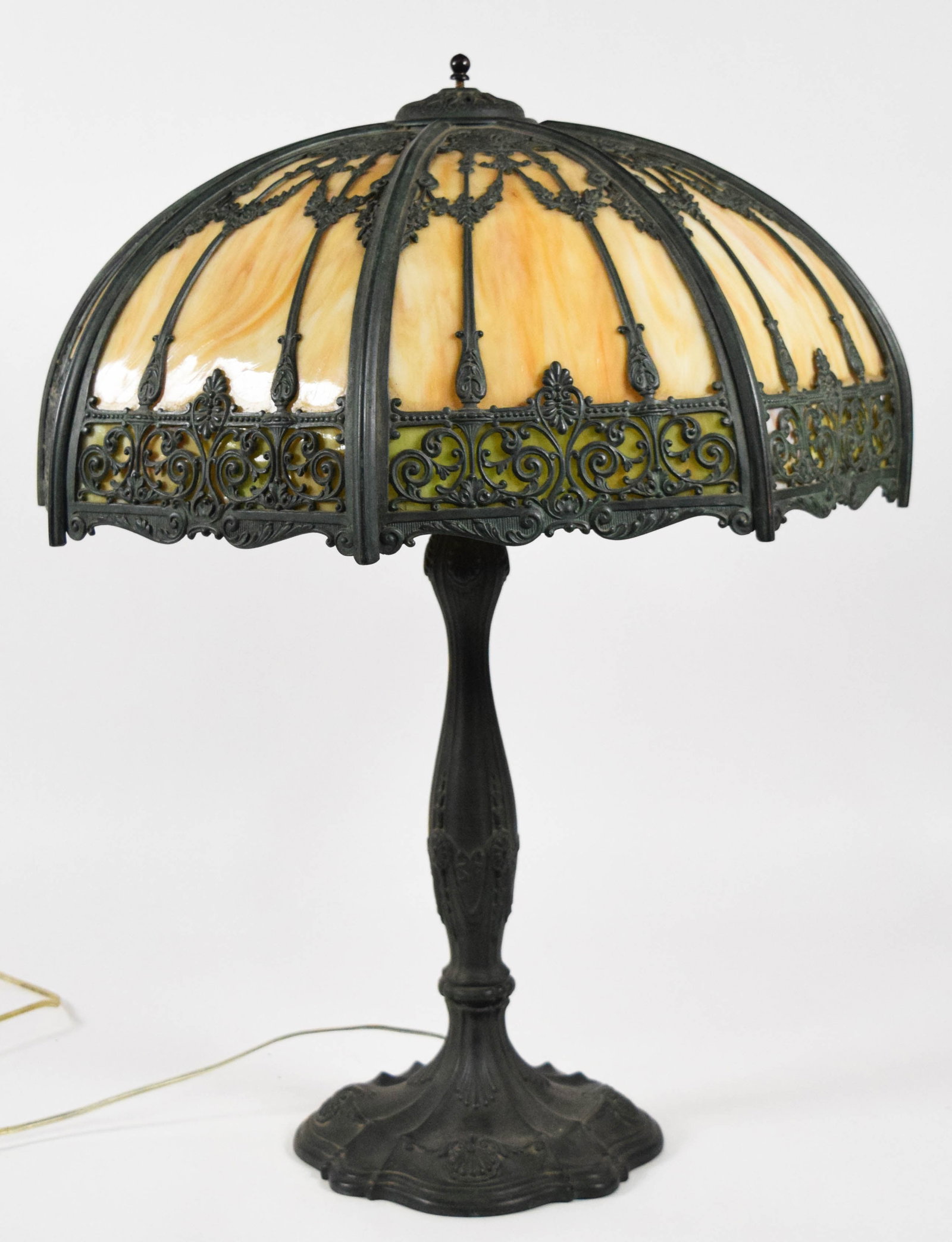 American Slag Glass and Patinated Metal Filigree Table Lamp: This table lamp features an eight-panel shade composed of caramel-colored slag glass upper panels and a lower border of green slag glass. The glass is set behind an ornate patinated metal filigree ove