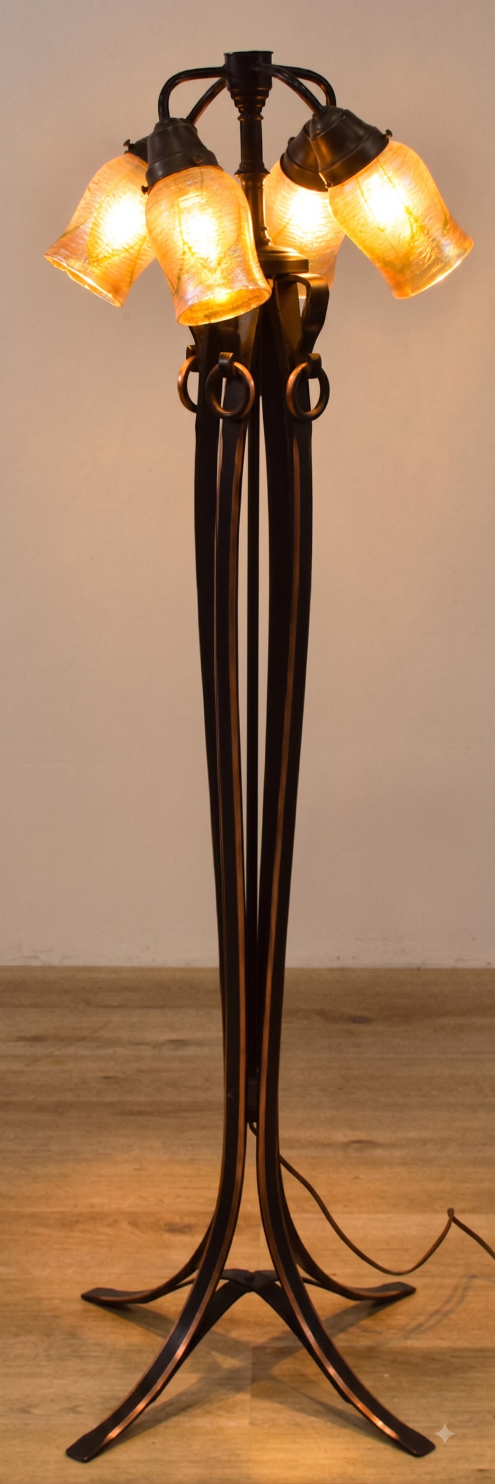 4-Light Wrought Iron Floor Lamp with Iridescent Art Glass Lily Shades: A 4-light floor lamp featuring a wrought iron frame with copper-toned metal accents in the Arts and Crafts style. The lamp stands on a four-legged base that rises into slender vertical elements gather