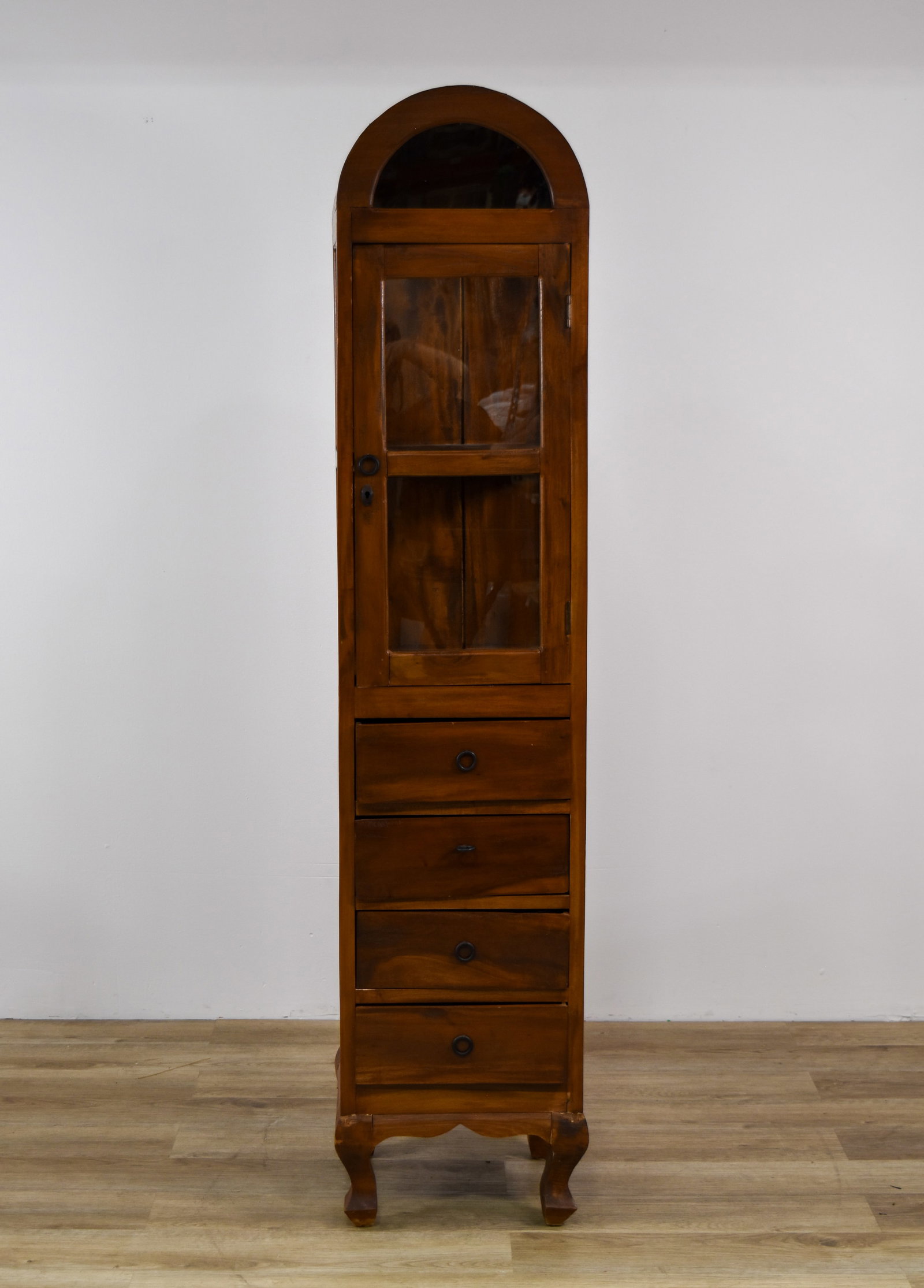 Slim Arched Top Wooden Display Cabinet with Four Drawers: A tall, one-piece slim curiosity cabinet, with a bonnet top featuring an arched glass panel and three-sided glazing in the upper display section. A single glass-paned door with a central horizontal mu