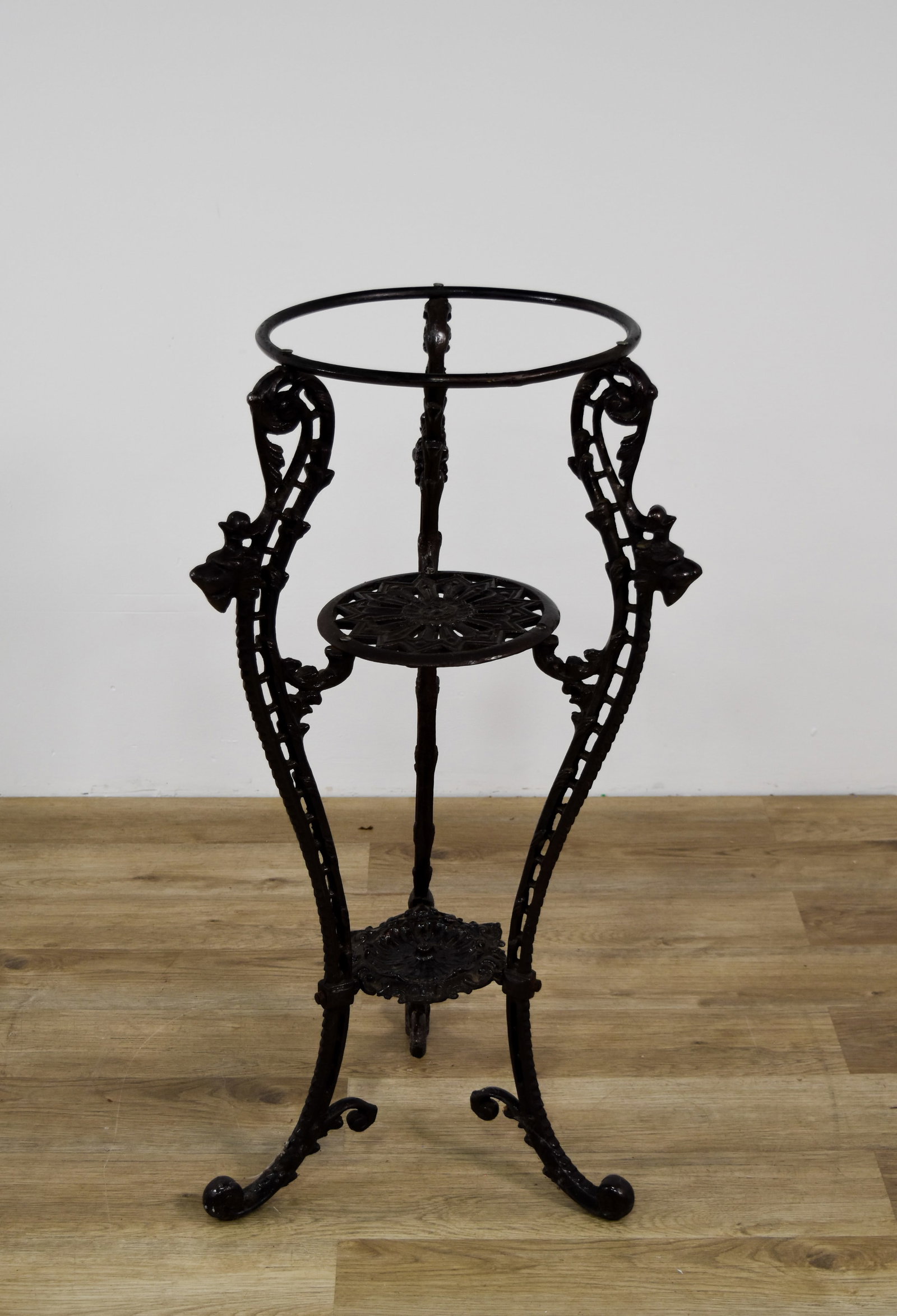 Victorian Style Three-Tier Cast Iron Plant Stand with Lion Head Motifs: A floor-standing cast iron plant stand featuring a three-tier tripod design. The frame is supported by three scrolling legs that terminate in rounded knobbed feet. The upper supports are decorated wit