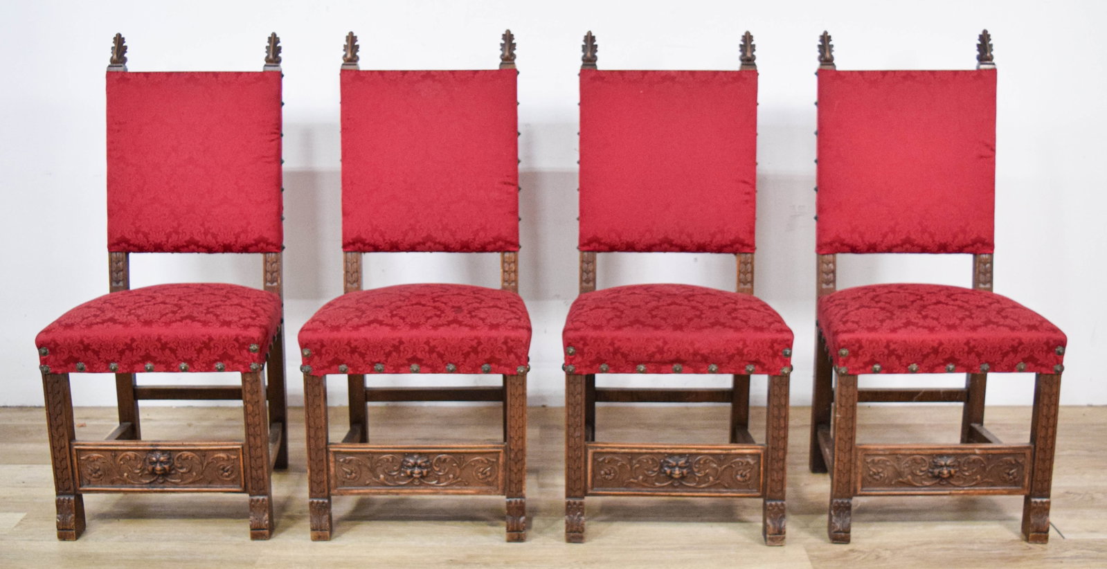 4 Jacobean Revival Style Carved Oak Side Chairs: Set of four Jacobean Revival style carved oak side chairs with red damask upholstery. Each chair with carved acanthus leaf finials and front stretchers carved with central grotesque masks and foliate