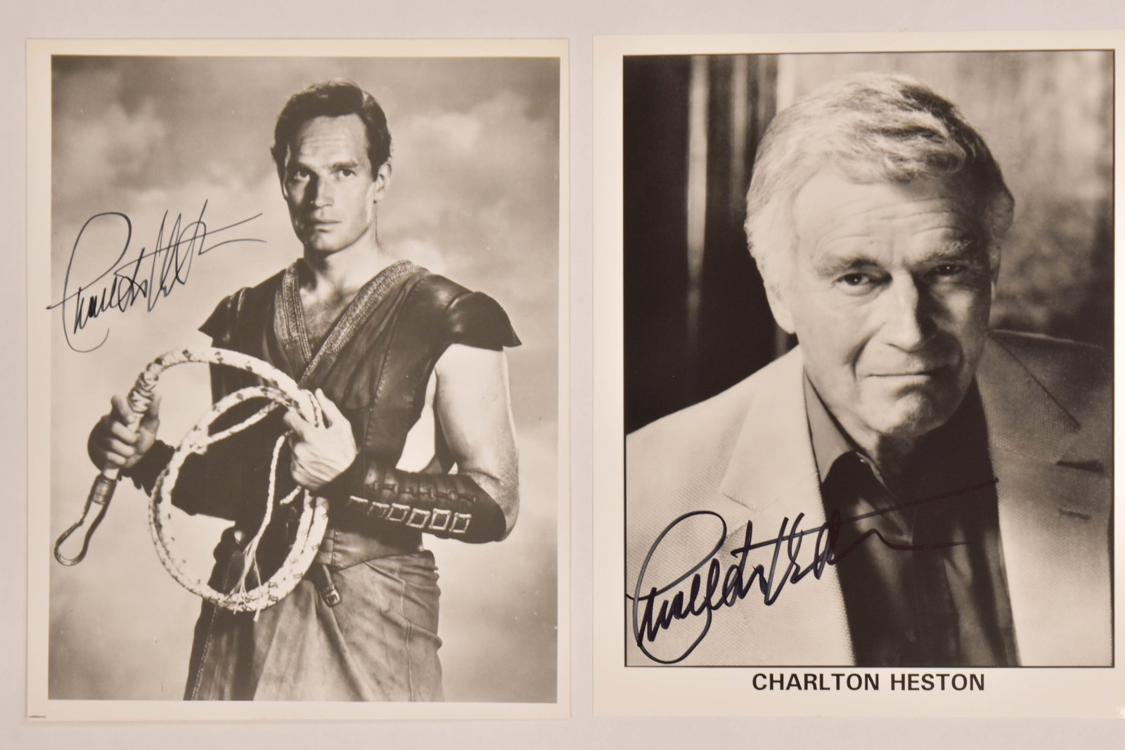 2 Charlton Heston Autographed Black and White Photographs: Charlton Heston (American, 1923-2008). 2 autographed black and white photographs. The first is a production still of the actor in a historical costume holding a coiled whip. The second is a headshot