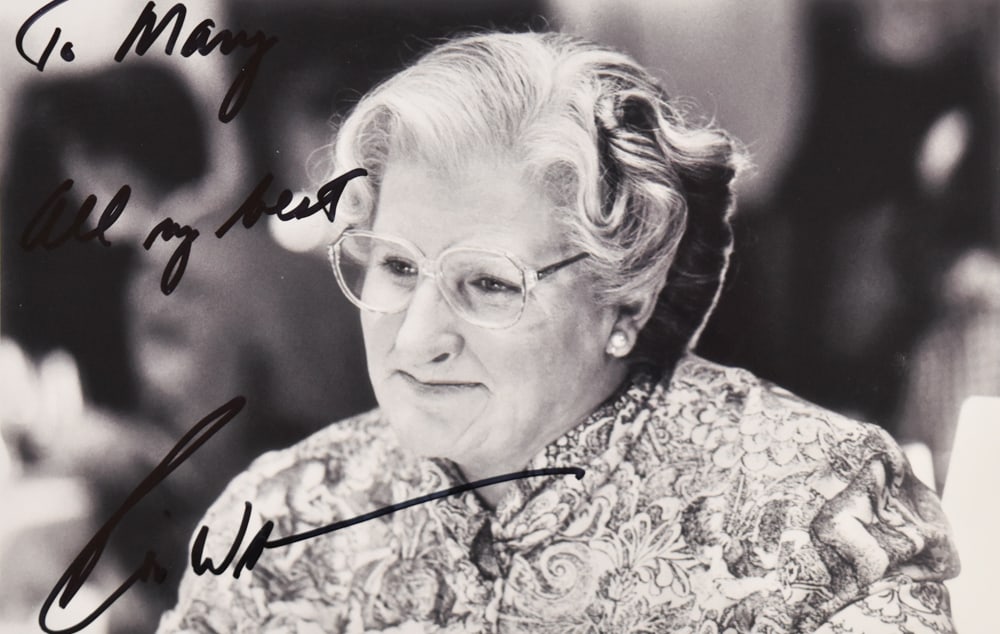 Robin Williams Autographed Photograph Mrs. Doubtfire: Robin Williams (American, 1951-2014). Black and white promotional photograph for the 1993 film Mrs. Doubtfire. The close-up portrait shows Williams in full character makeup, wearing spectacles and a f