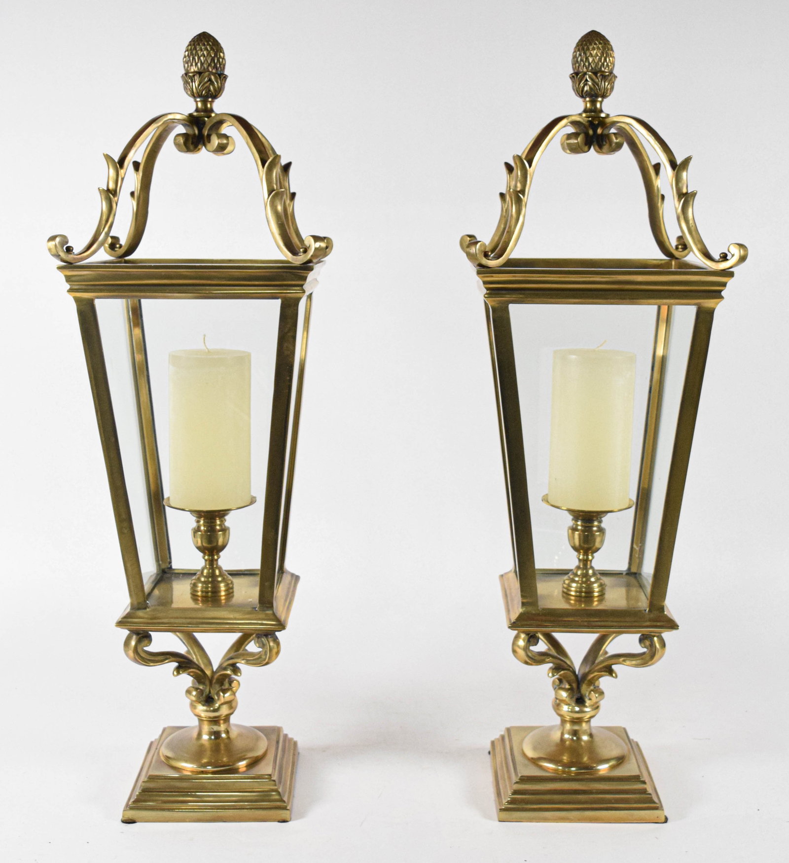 Pair of Neoclassical Revival Brass and Glass Tabletop Candle Lanterns: Pair of large neoclassical revival style tabletop candle lanterns constructed of polished brass and clear glass. Each lantern features a tapered rectangular form with clear glass panes set into brass 