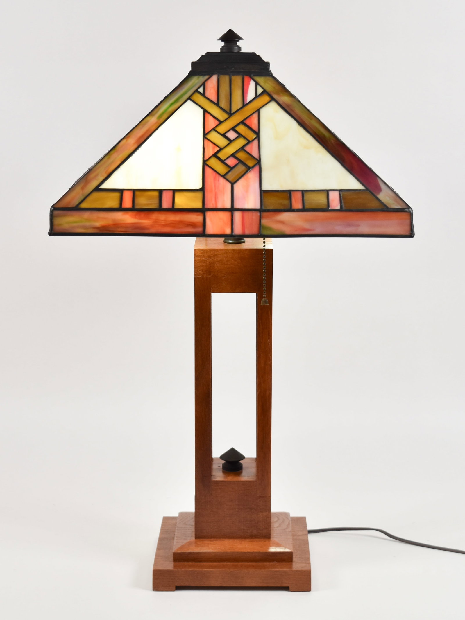 Mission Style Stained Glass Table Lamp: Mission style table lamp featuring a geometric leaded glass shade and a stained wood base. The pyramidal shade is composed of slag glass panels in a palette of cream, amber, and earth tones, accented 