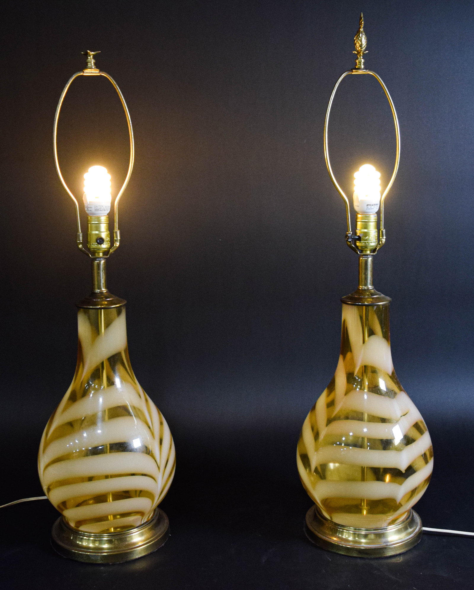 Pair of Mid Century Modern Hand Blown Amber Glass Table Lamps: Pair of MCM hand-blown glass table lamps. The translucent honey-amber glass is decorated with an opaque cream-colored pulled feather swirl pattern throughout. The glass components are mounted on circu