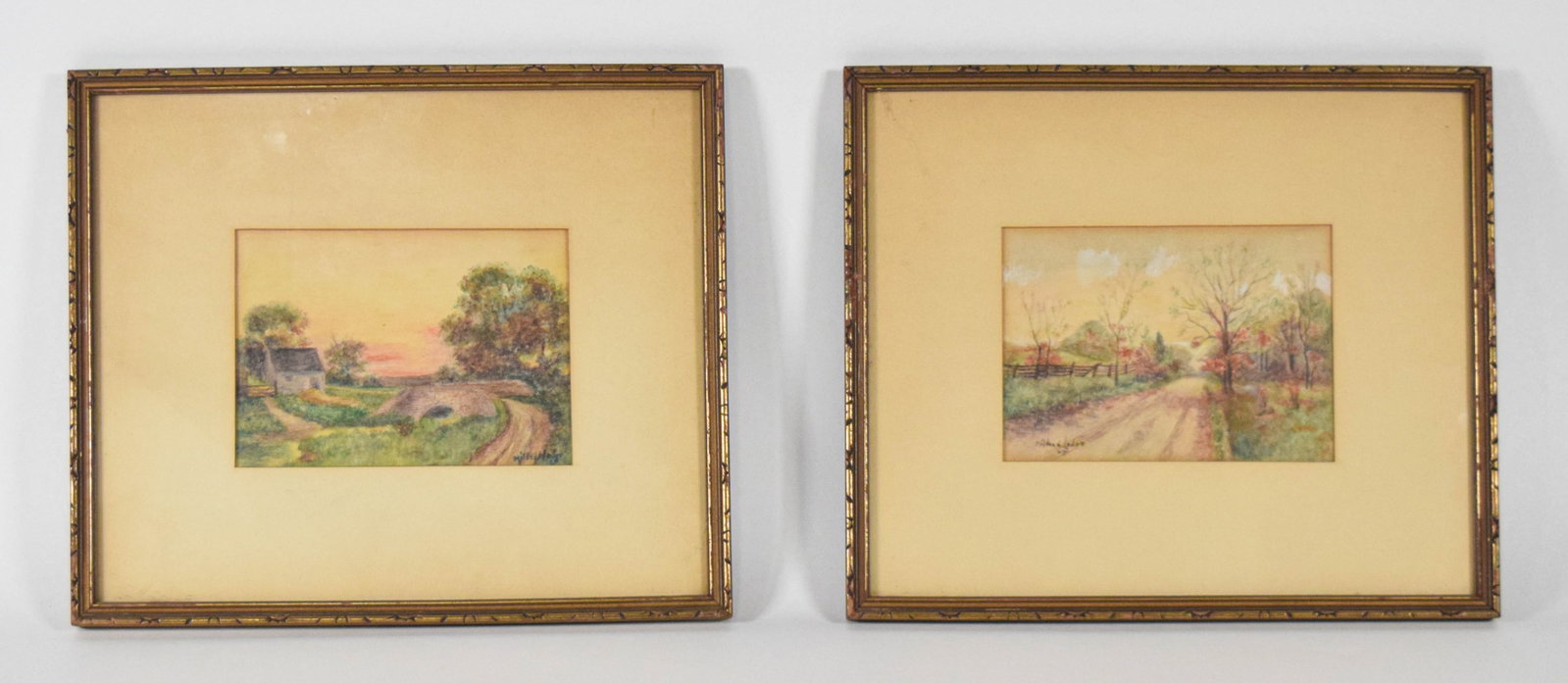 Mildred Leder Pair of Watercolor Landscapes: A pair of 20th-century watercolor paintings on paper by Mildred Leder. The first composition features a rural scene with a small stone cottage and a single-arch stone bridge set against a sunset sky w