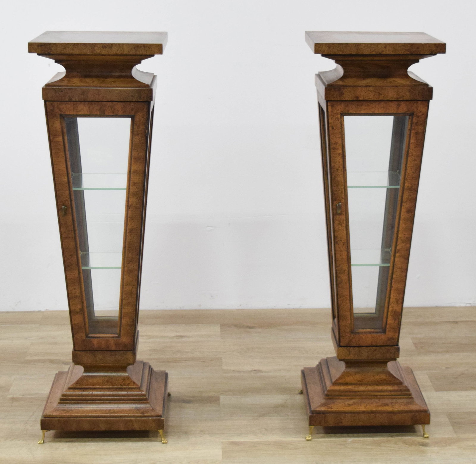 Pair of Empire Revival Burl Wood Vitrine Pedestal Display Cases: Pair of Empire Revival style vitrine pedestal display cases featuring burl wood veneer. Each piece is designed with a neoclassical aesthetic, displaying an antiqued finish with intentional fly-specked