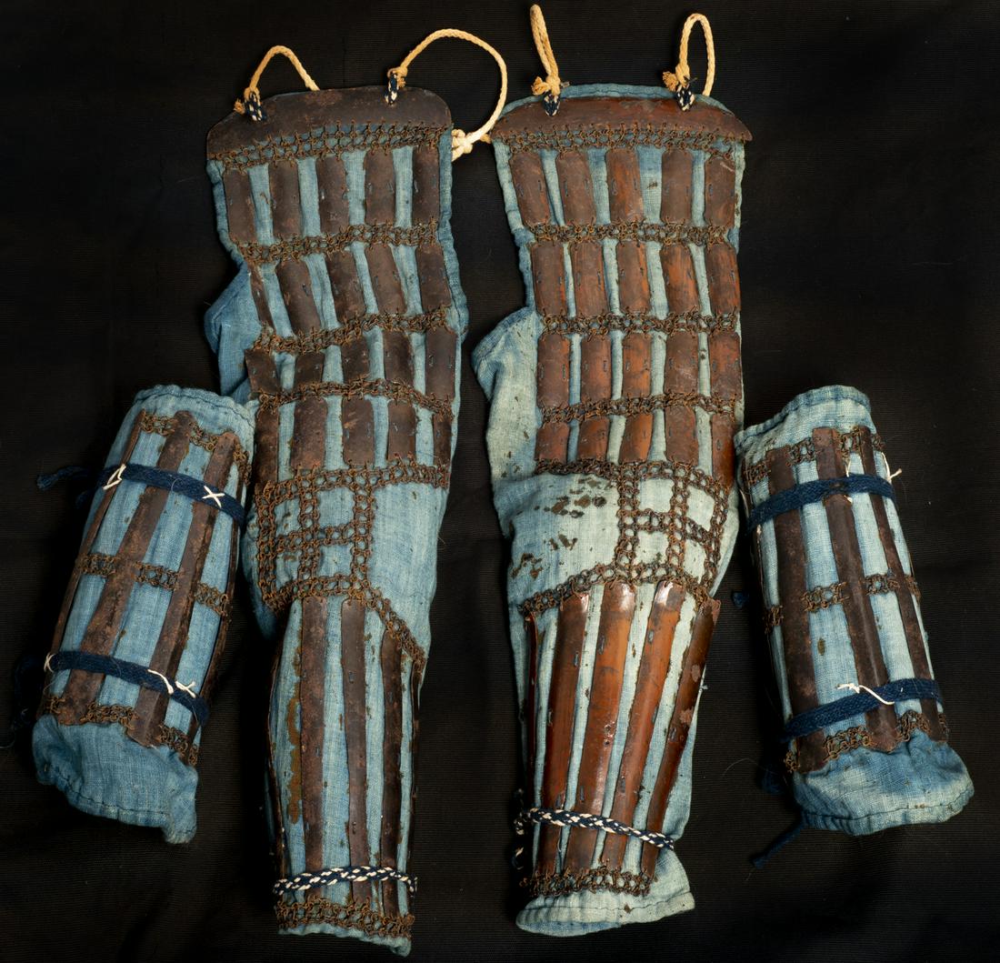 Set of Japanese Kusari and Sune-Ate: Lot consists of one set of Japanese tekko (arm guards) and sune-ate (shin guards). Both of lacquered iron sewn to light blue textile backing. Tekko measure 23.5" x 7", sune-ate measure 11" x 4.5". **S