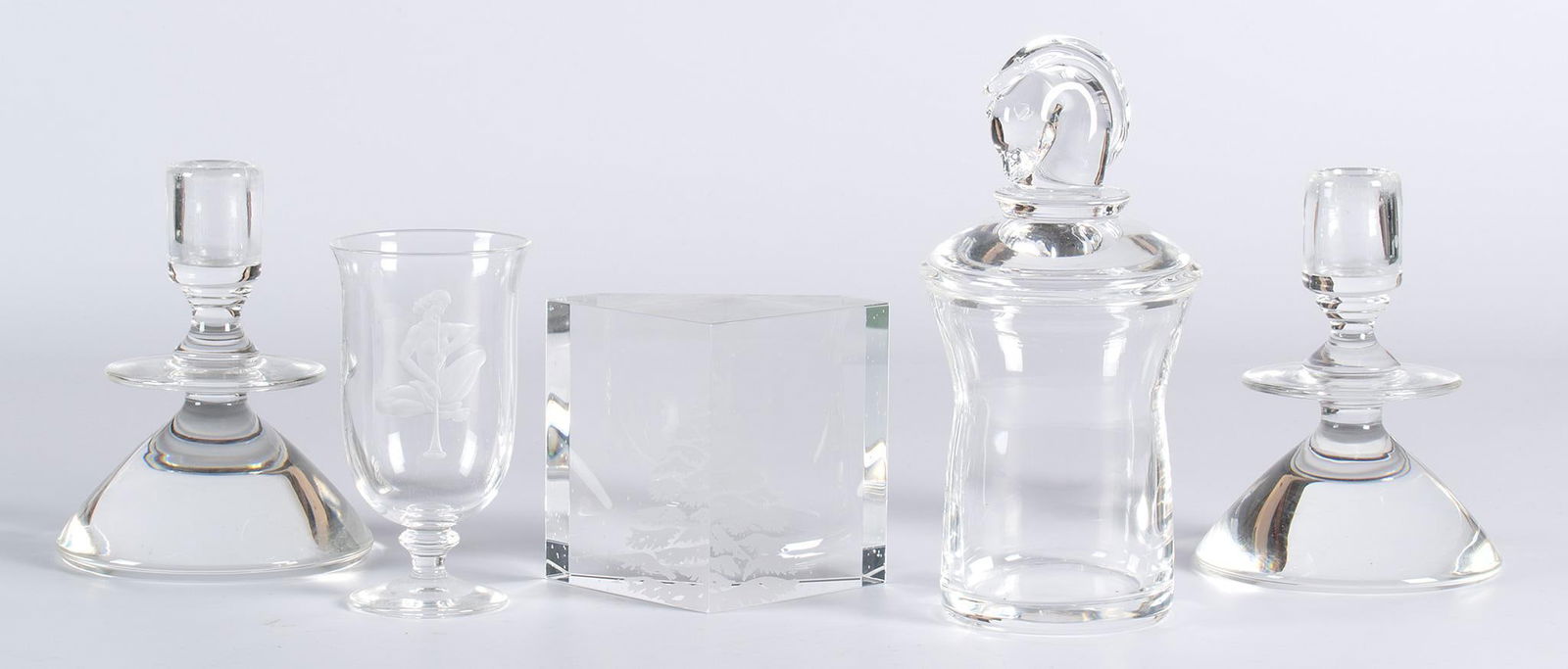 A Group of Steuben Tablewares: American, 20th century. A grouping of 5 Steuben crystal tablewares, lot includes a etched Christmas tree sculpture, two lidded jars (one with etched nude figure), and two candlesticks, all marked Steu